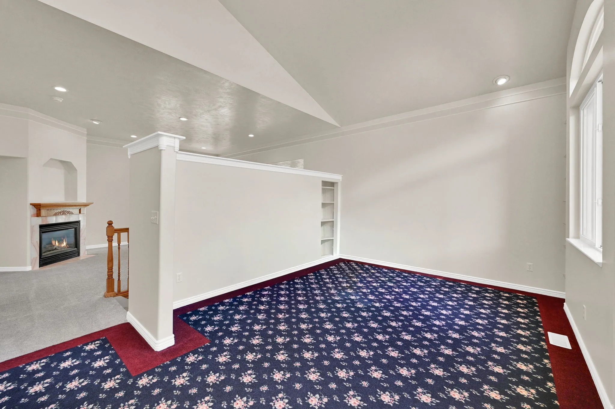 Spacious room with patterned carpeting, white walls, and a built-in bookshelf