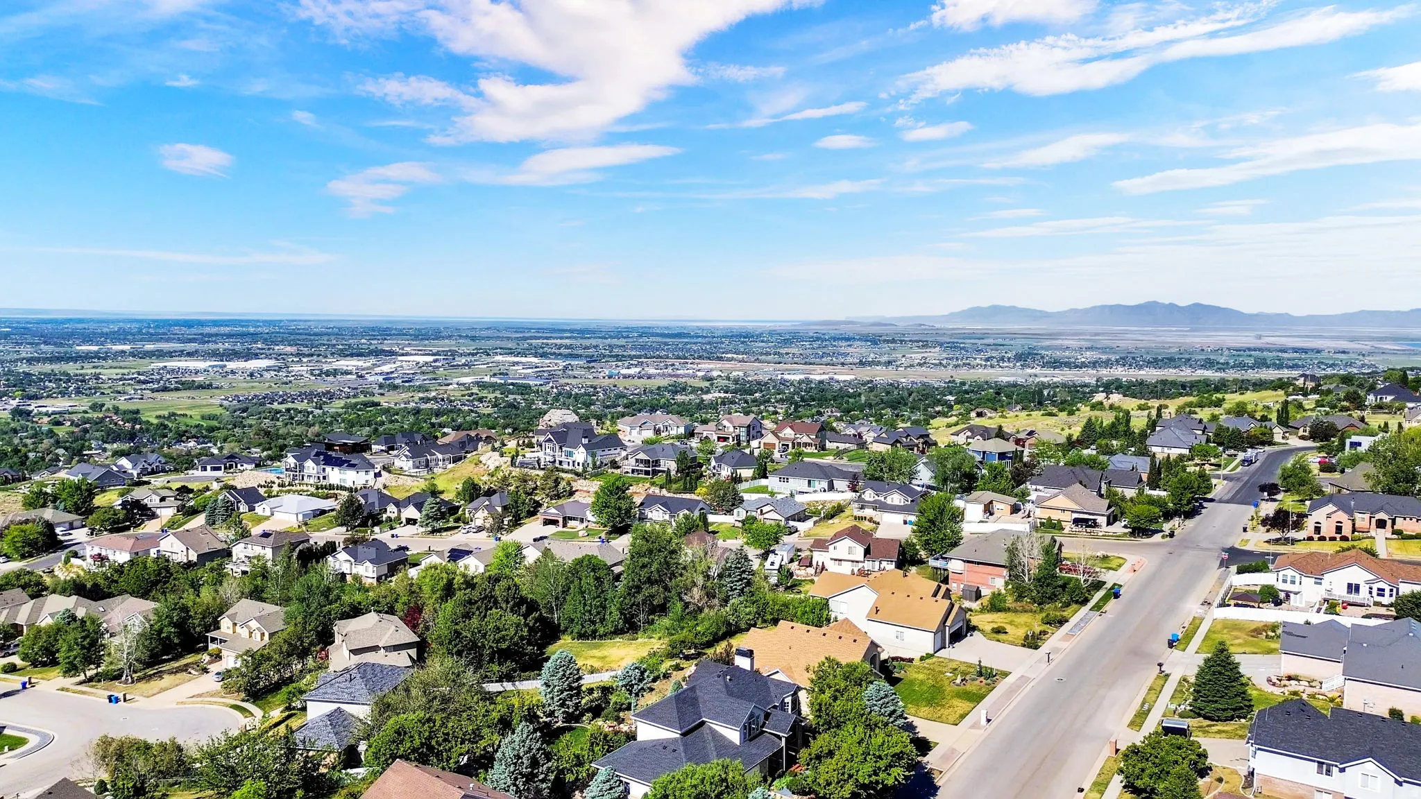 Expansive neighborhood featuring varied residential properties, mature trees, and paved streets, all set against a distant mountain range