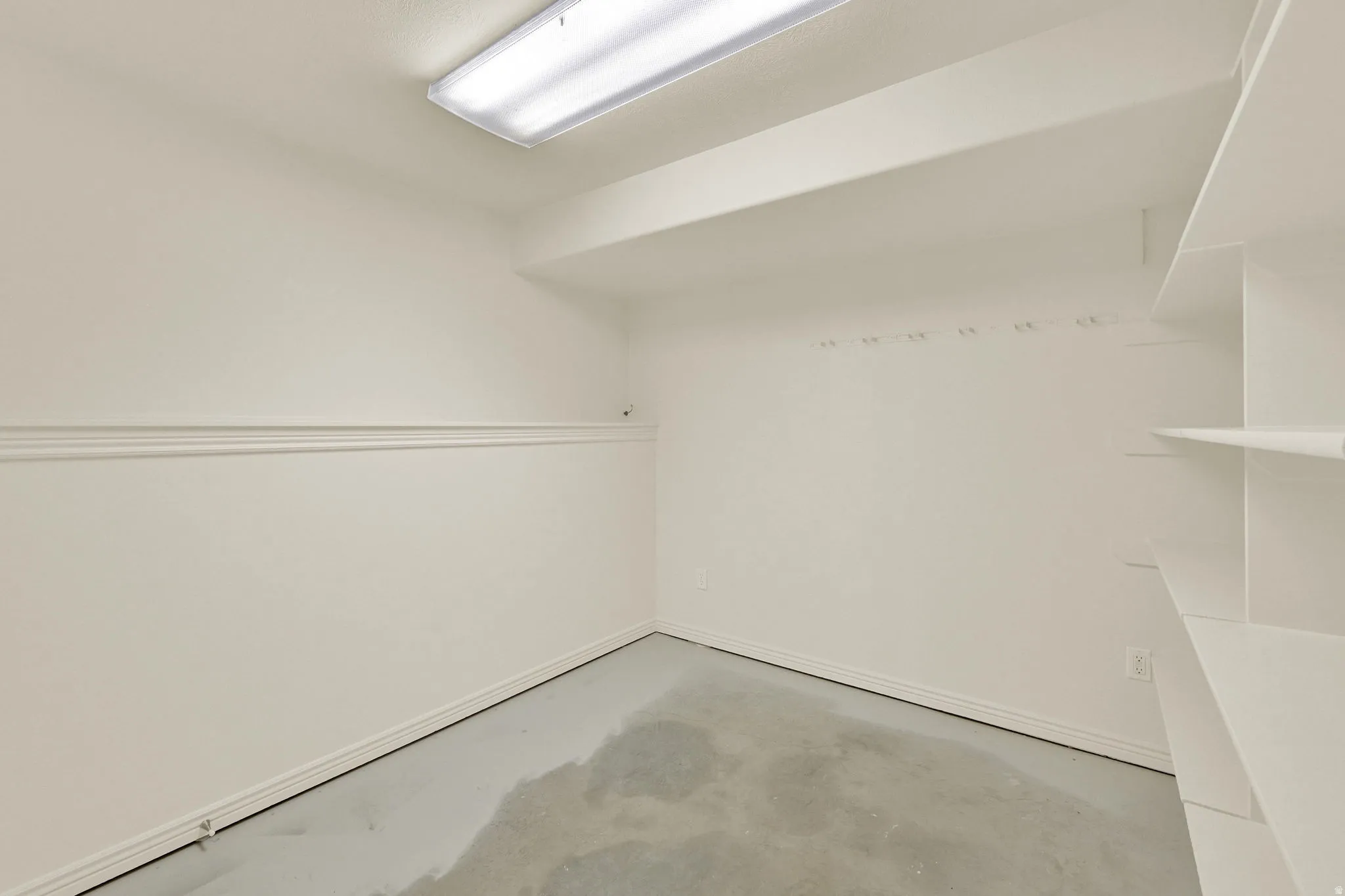 Utility room featuring built-in shelving, wall-mounted hooks, baseboard trim, and overhead fluorescent lighting