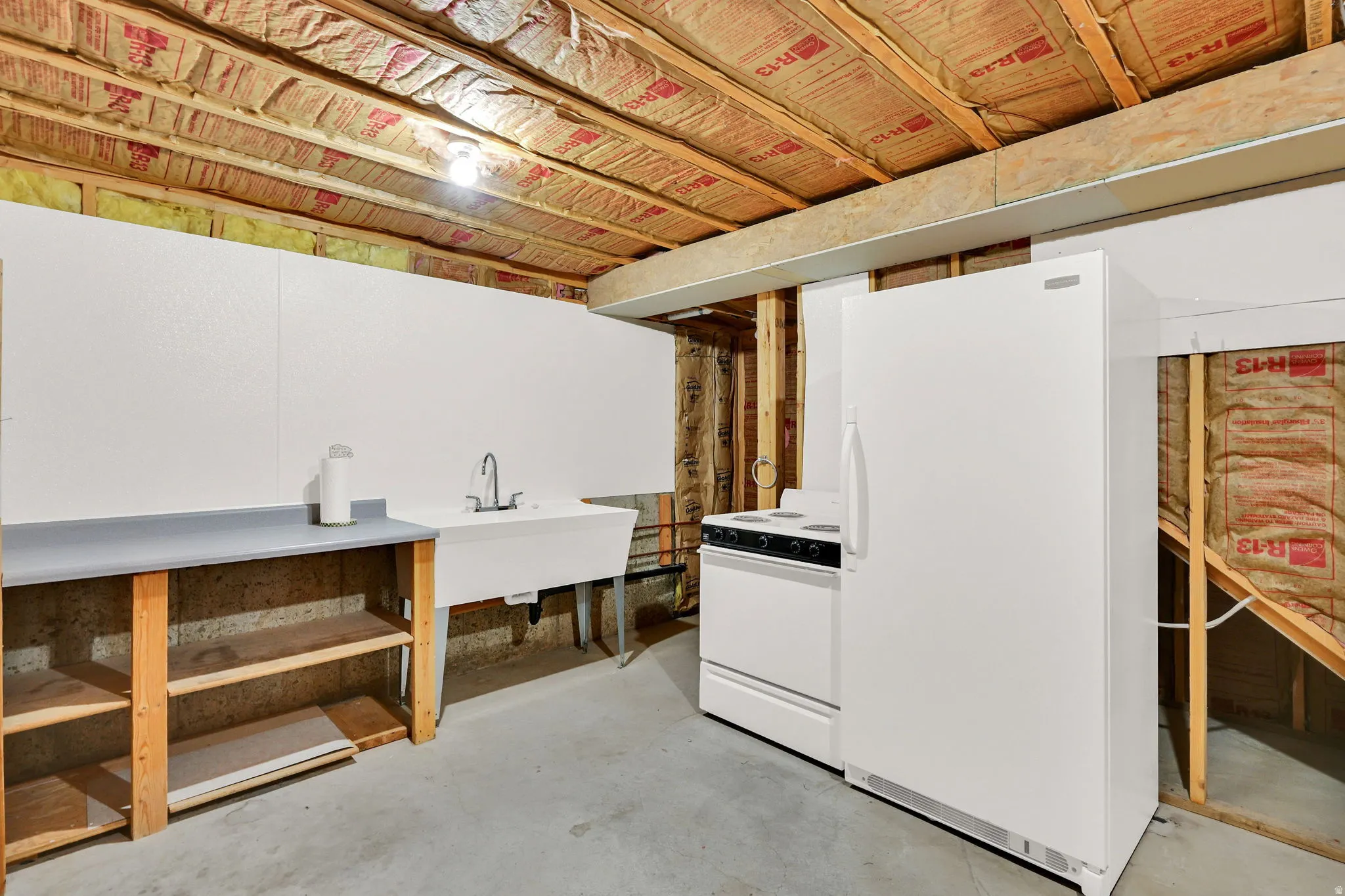 Utility area featuring a white laundry sink with a chrome faucet, a white freestanding range, a white refrigerator, and a built-in wooden shelving unit with a gray countertop