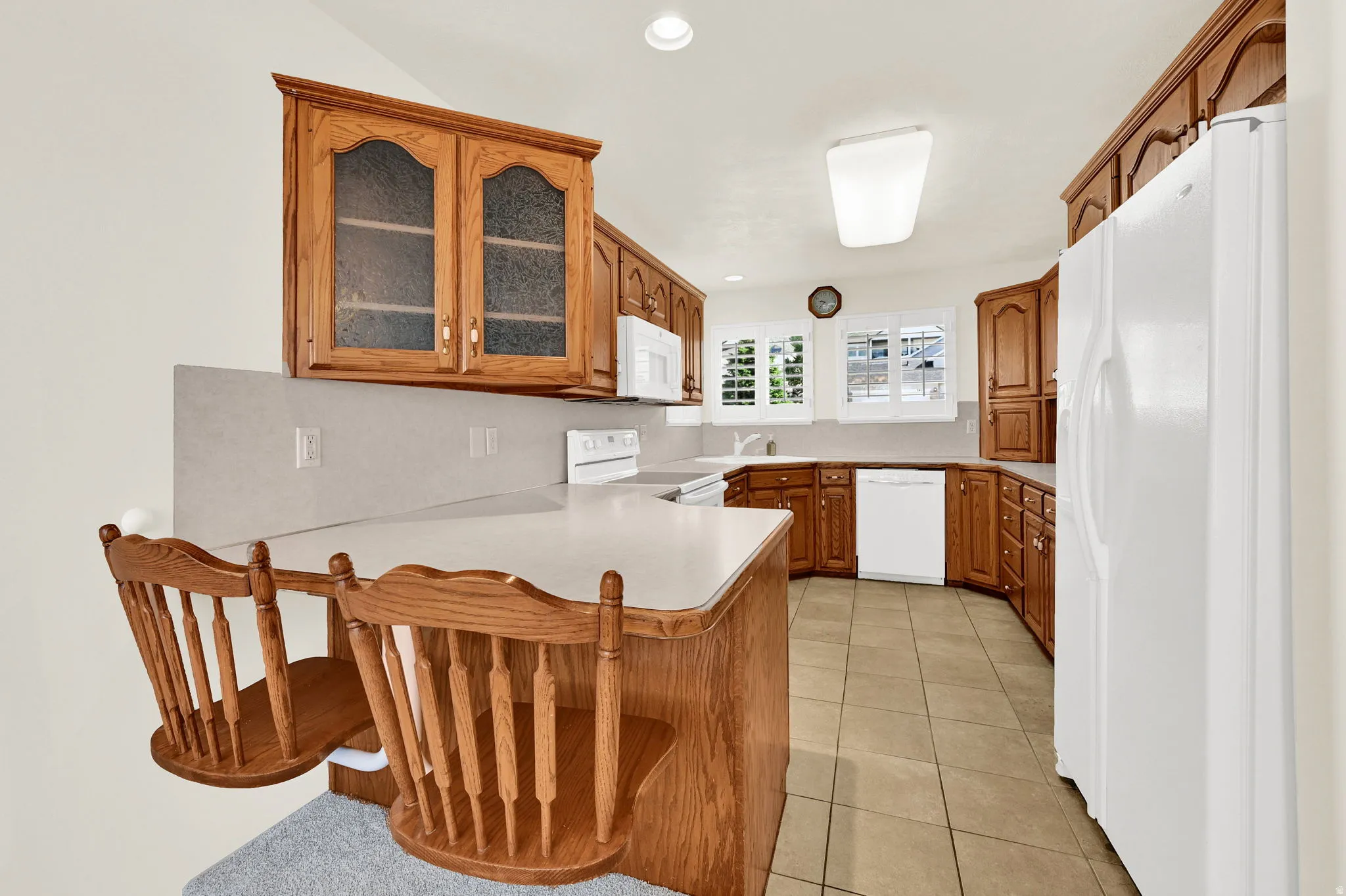 Kitchen featuring wood cabinetry, white appliances, a breakfast bar, and tile flooring