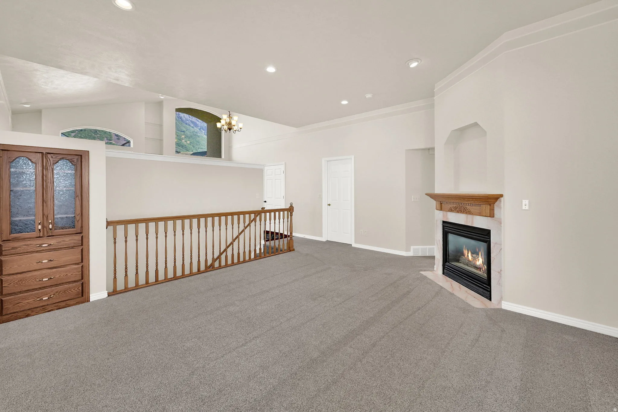 Spacious room with light gray carpeting and a gas fireplace featuring a wood mantel and stone surround