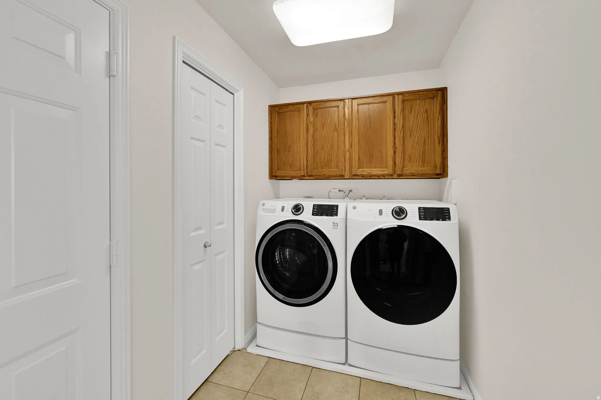 Dedicated laundry area with upper wood cabinetry and tile flooring