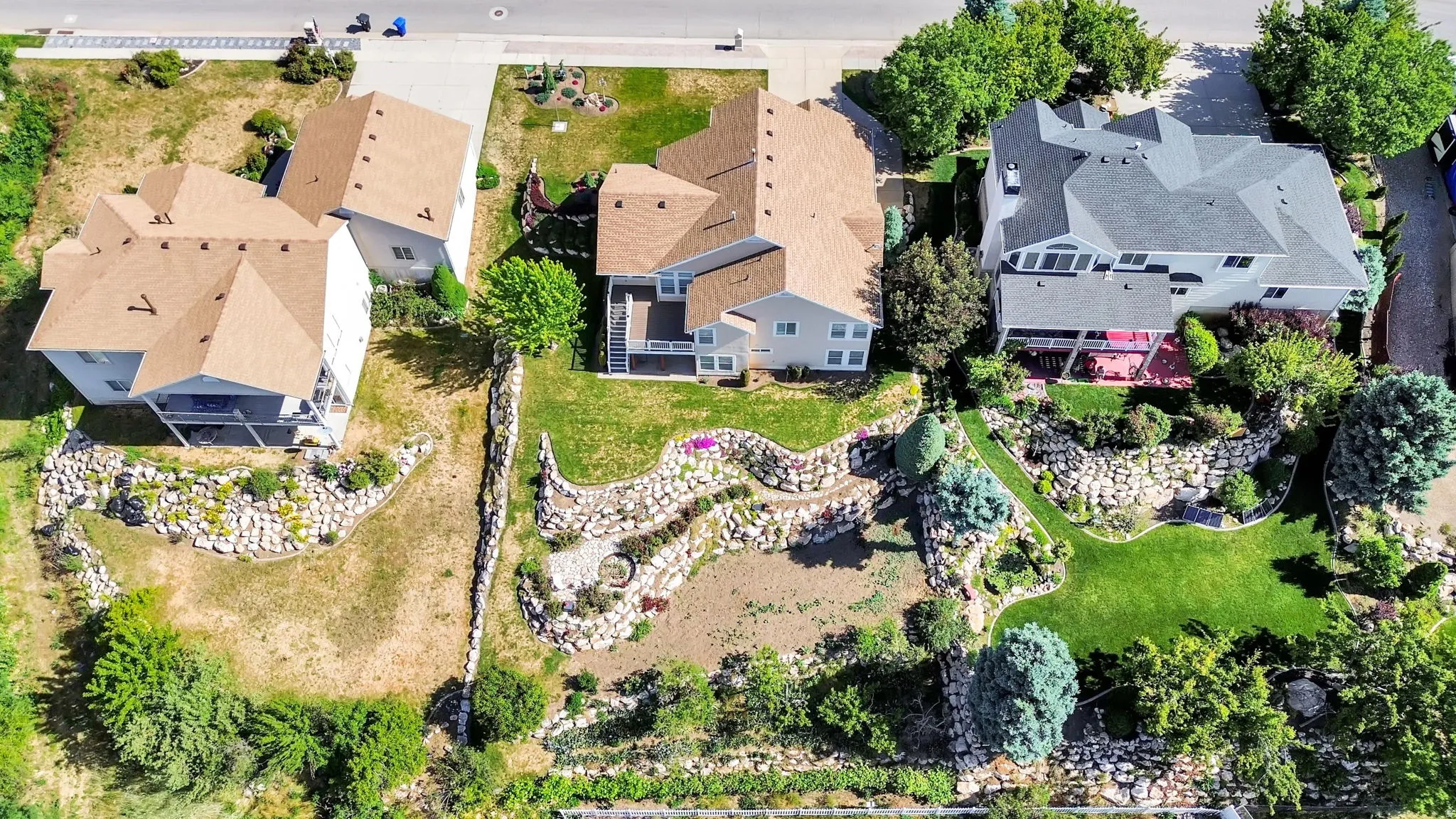 Expansive terraced backyard featuring rock retaining walls, mature trees, and a manicured lawn area