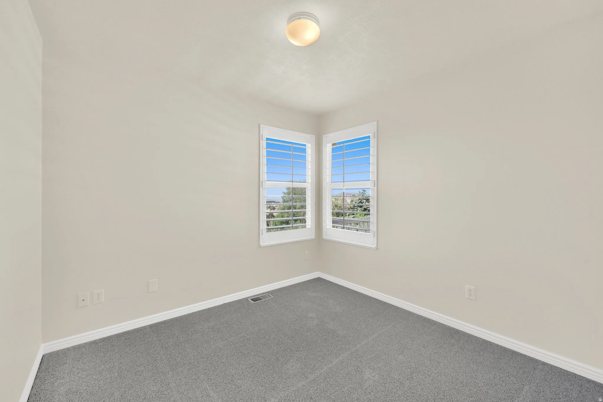 Corner windows with plantation shutters, light-toned walls, and grey carpeting