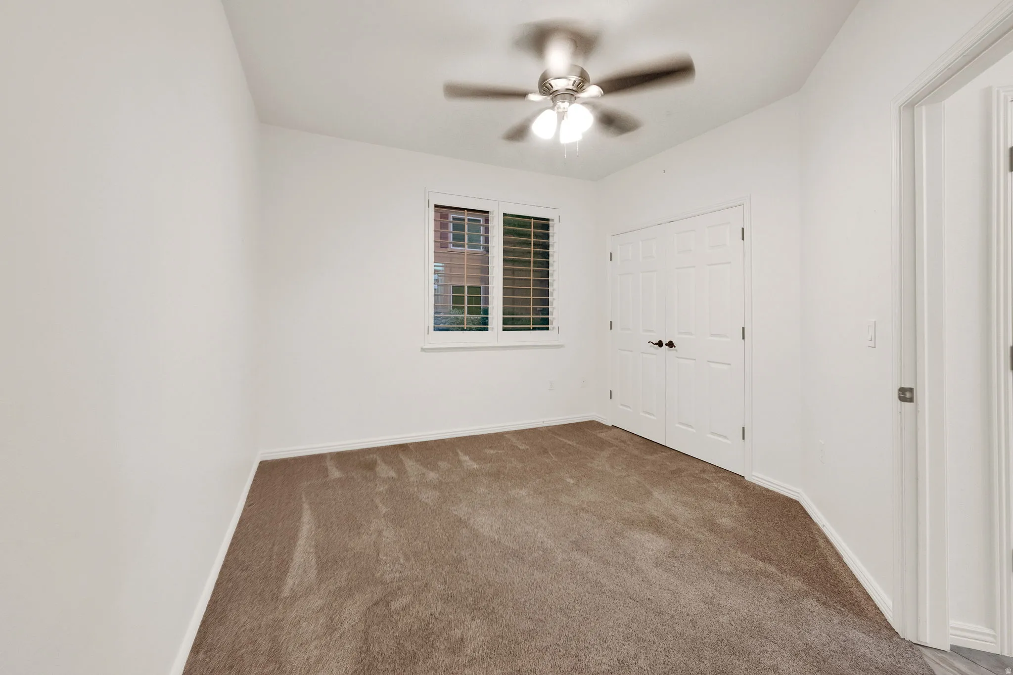 Bedroom featuring neutral carpeting, a ceiling fan with integrated lighting, window with plantation shutters, and a double-door closet with black hardware