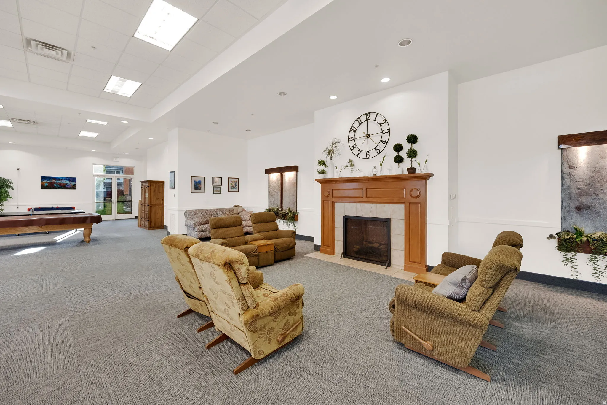 Spacious common area featuring a central fireplace with wood mantel and tile surround, recessed lighting, and large windows with natural light