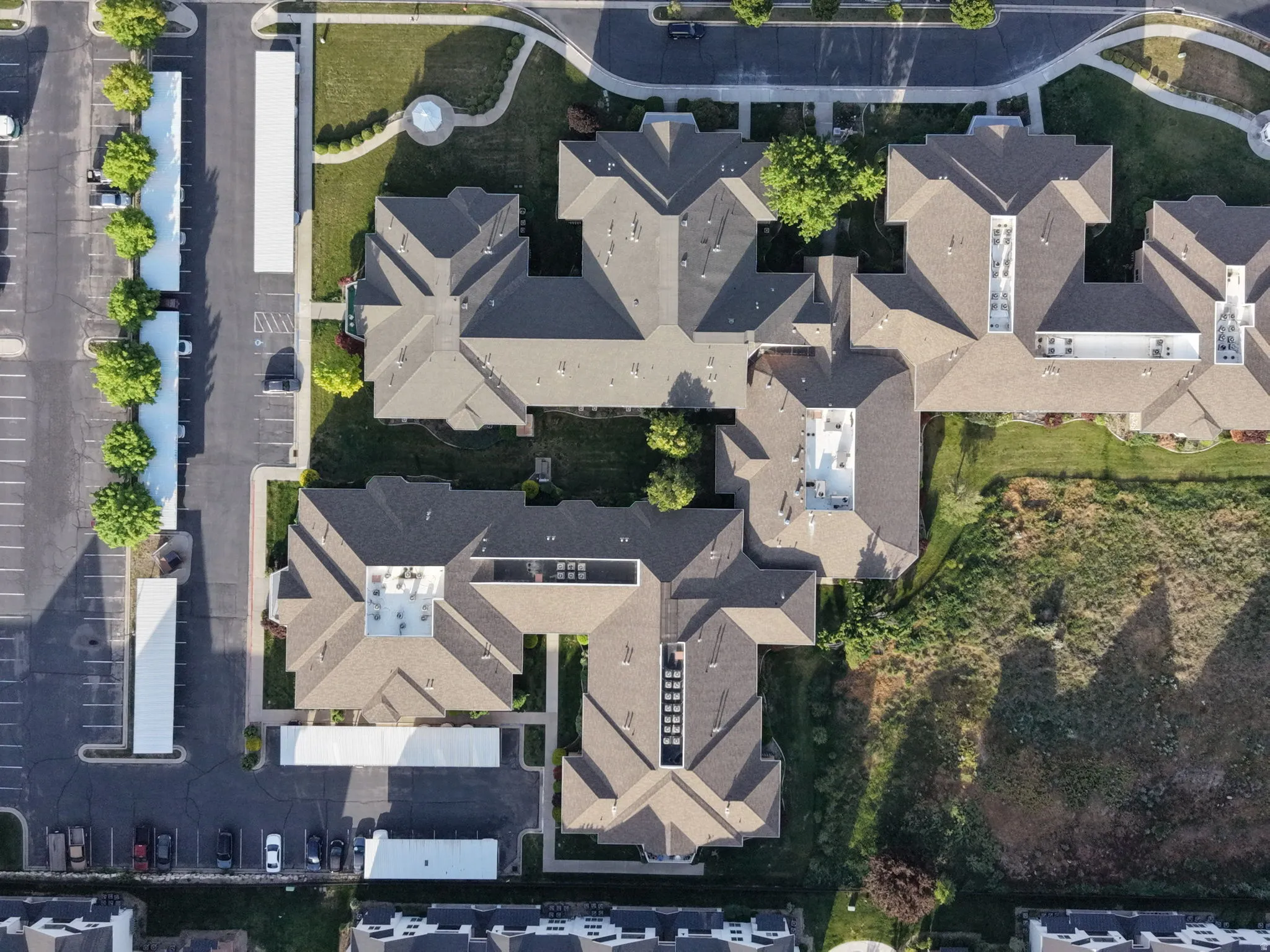 Aerial perspective showcasing multiple buildings with pitched roofs, surrounded by paved parking areas, covered parking structures, and landscaped green spaces