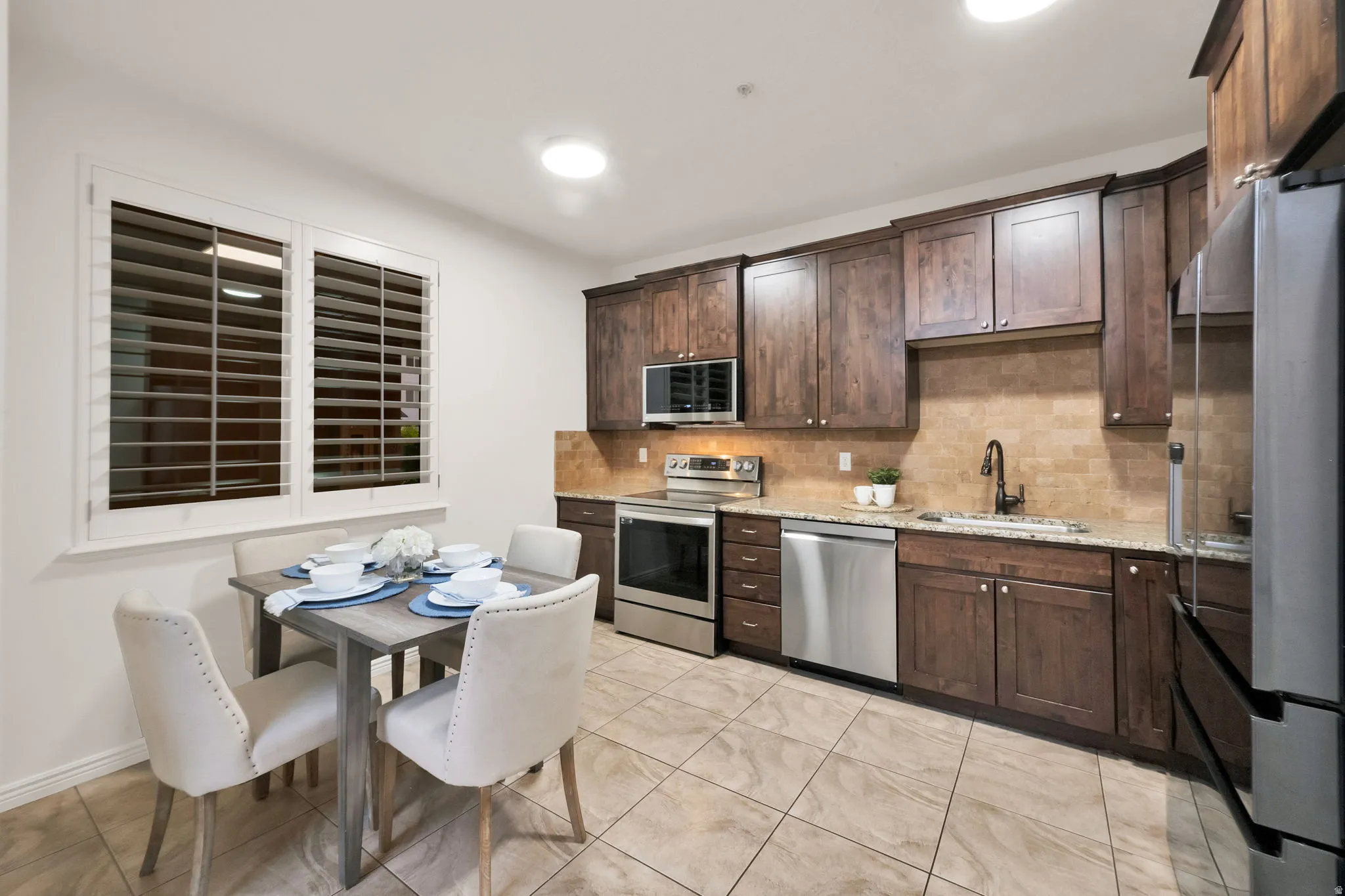 Kitchen area featuring wood-finish cabinetry, granite countertops, and stainless steel appliances including a refrigerator, dishwasher, and range with microwave