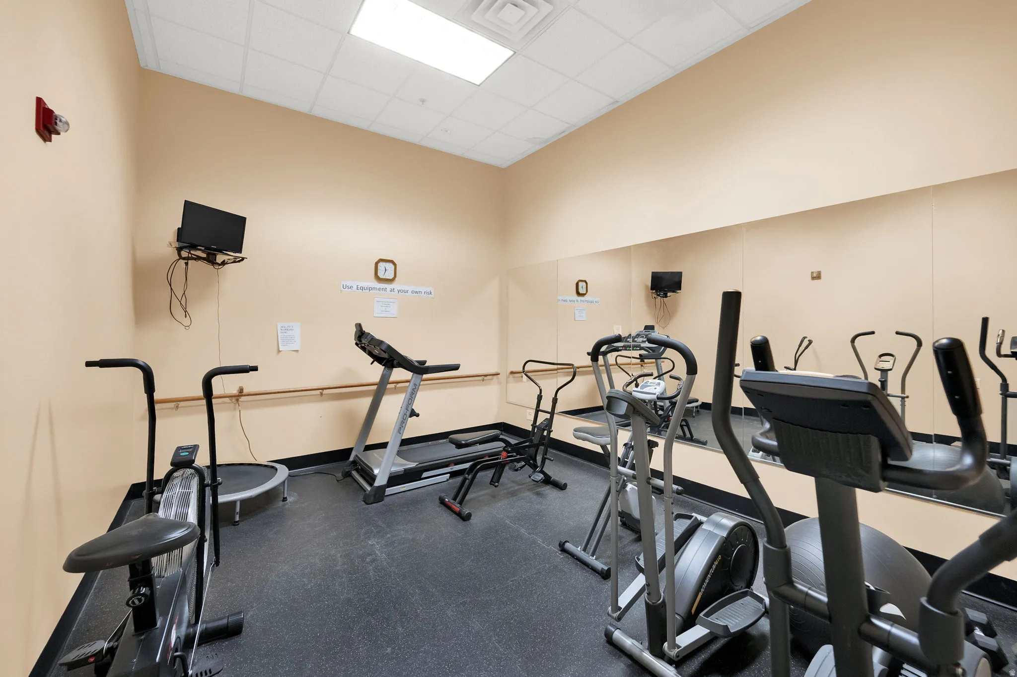 Dedicated fitness area featuring durable black rubber flooring, full-wall mirror, and a wall-mounted television
