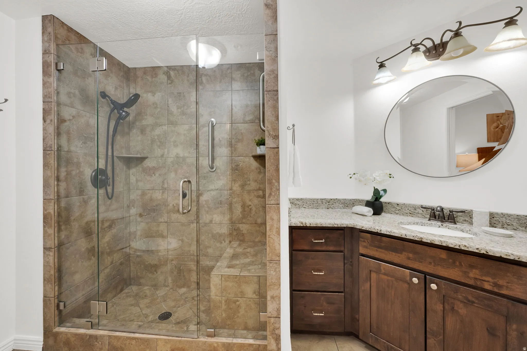 Shower with glass enclosure and tiled walls, featuring a built-in bench and recessed shelf