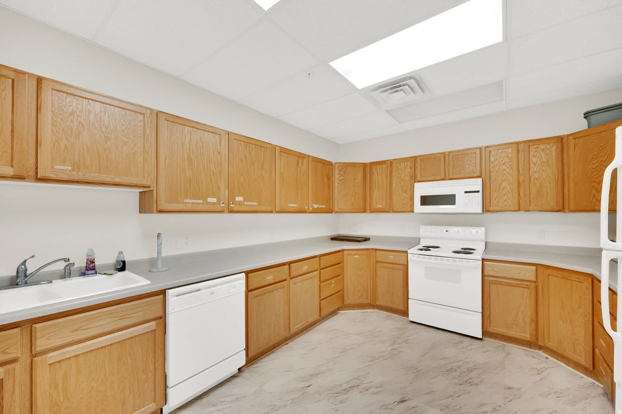 Kitchen featuring extensive light wood cabinetry, a white double basin sink, white dishwasher, white electric range with a matching over-range microwave, and light-toned flooring