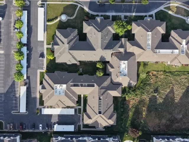 Aerial perspective showcasing multiple buildings with pitched roofs, surrounded by paved parking areas, covered parking structures, and landscaped green spaces