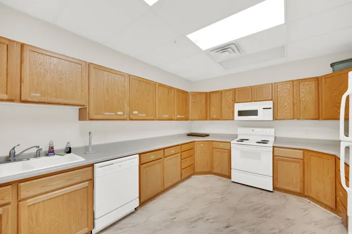Kitchen featuring extensive light wood cabinetry, a white double basin sink, white dishwasher, white electric range with a matching over-range microwave, and light-toned flooring