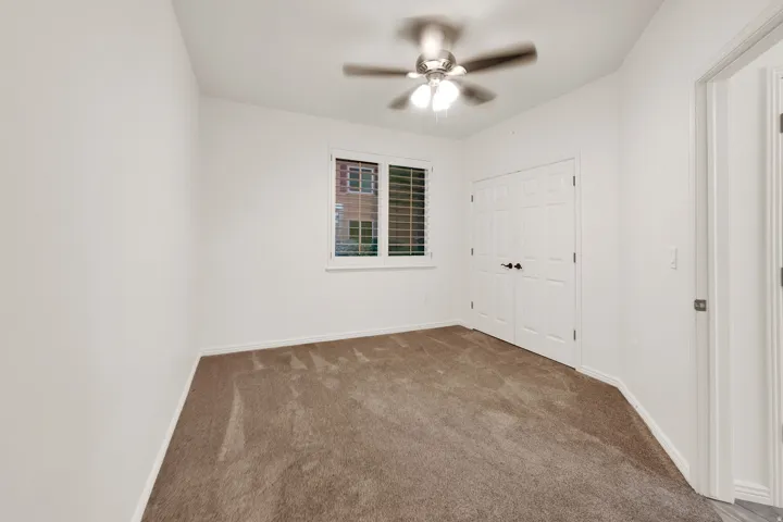 Bedroom featuring neutral carpeting, a ceiling fan with integrated lighting, window with plantation shutters, and a double-door closet with black hardware