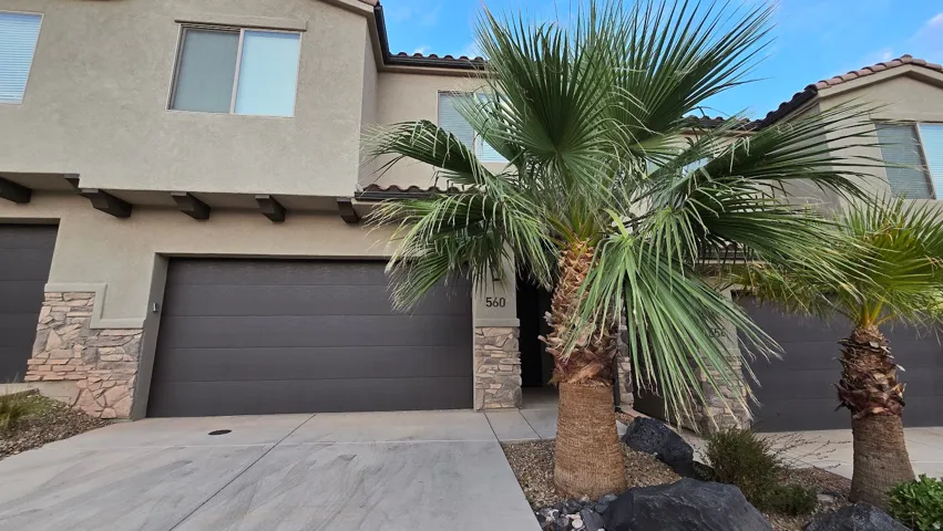Stucco exterior featuring stacked stone accents, a tile roof, and mature palm trees