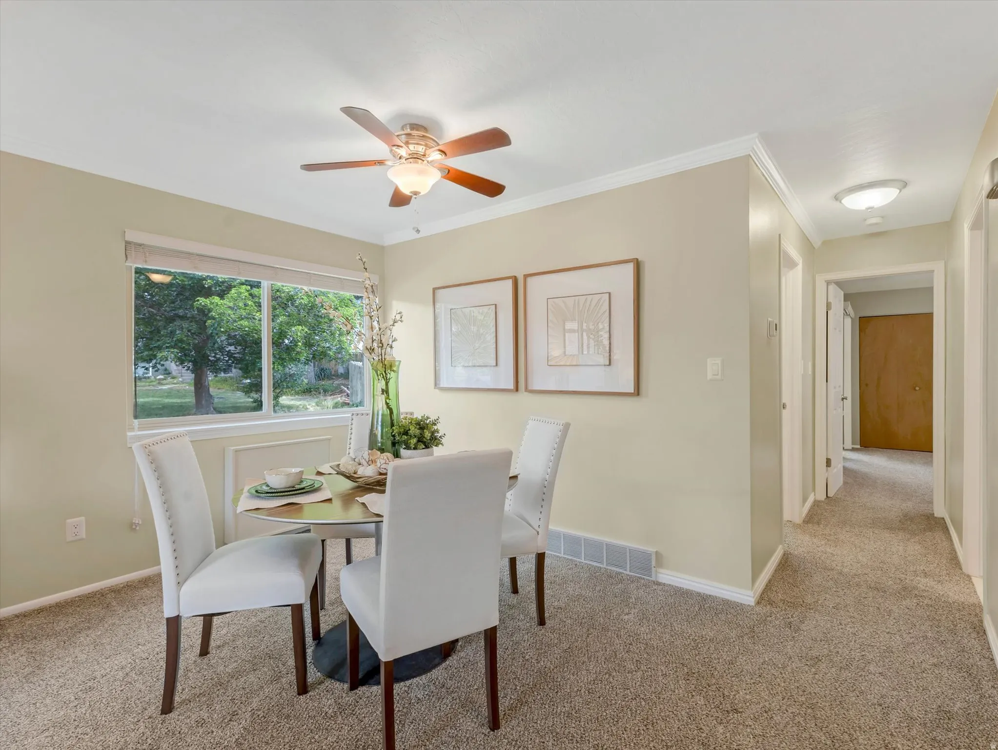 Dining area featuring a window with exterior views, crown molding, a ceiling fan with light fixture, and neutral-toned carpeting