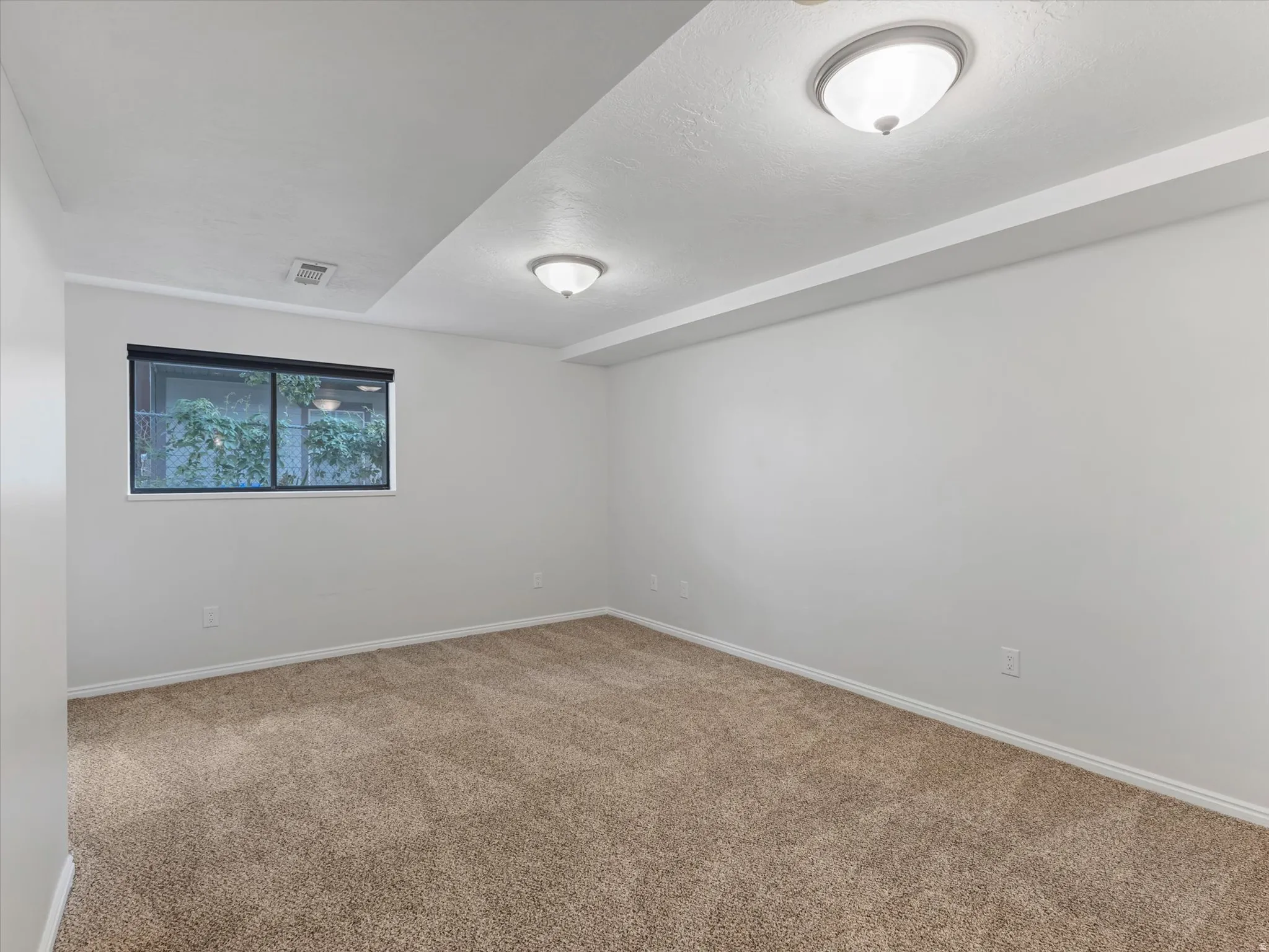 Neutral wall color with recessed ceiling beams, brown carpeting, and a window with a roller shade