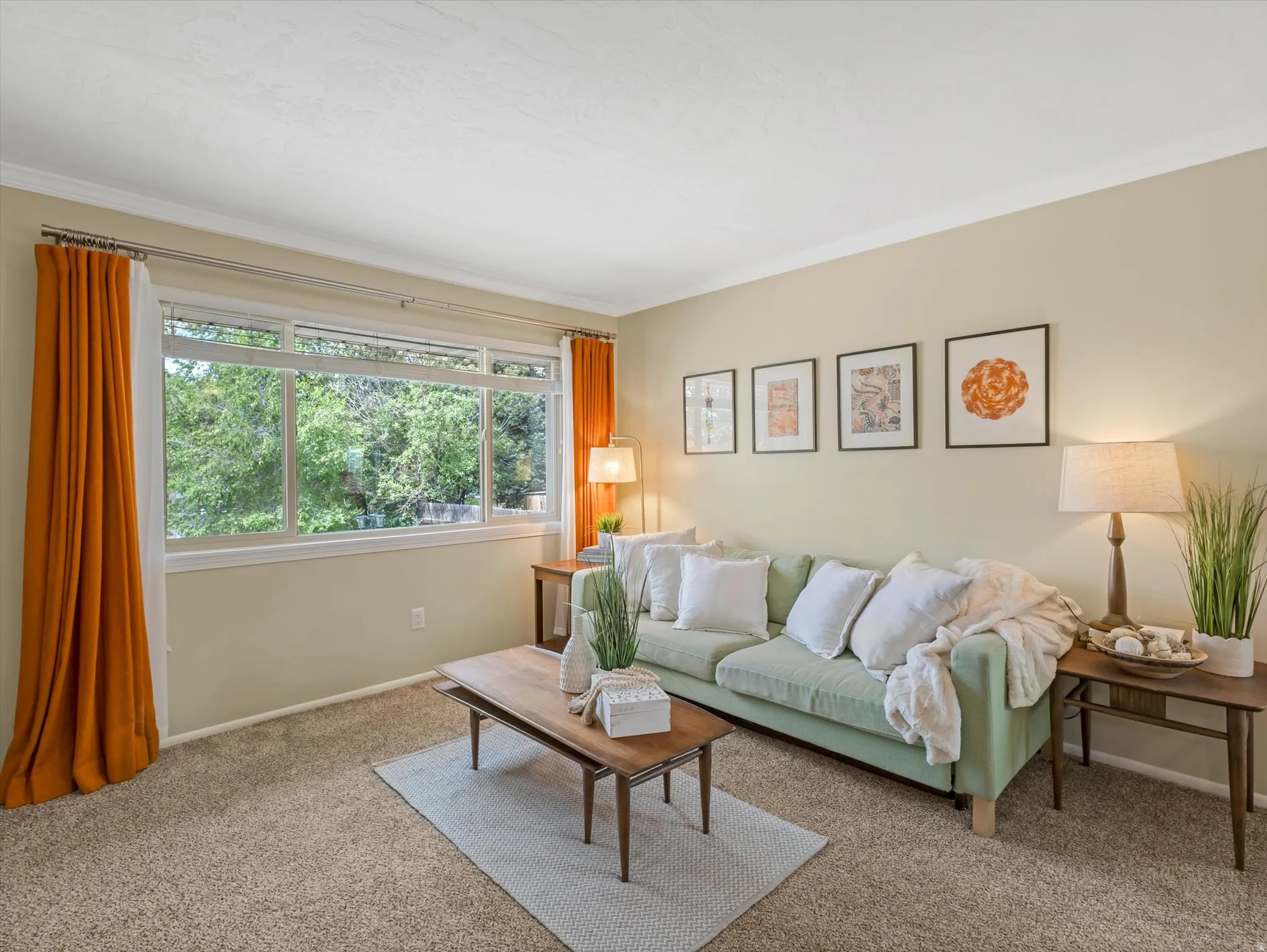 Living area featuring broad window, light beige wall color, crown molding, and carpet flooring