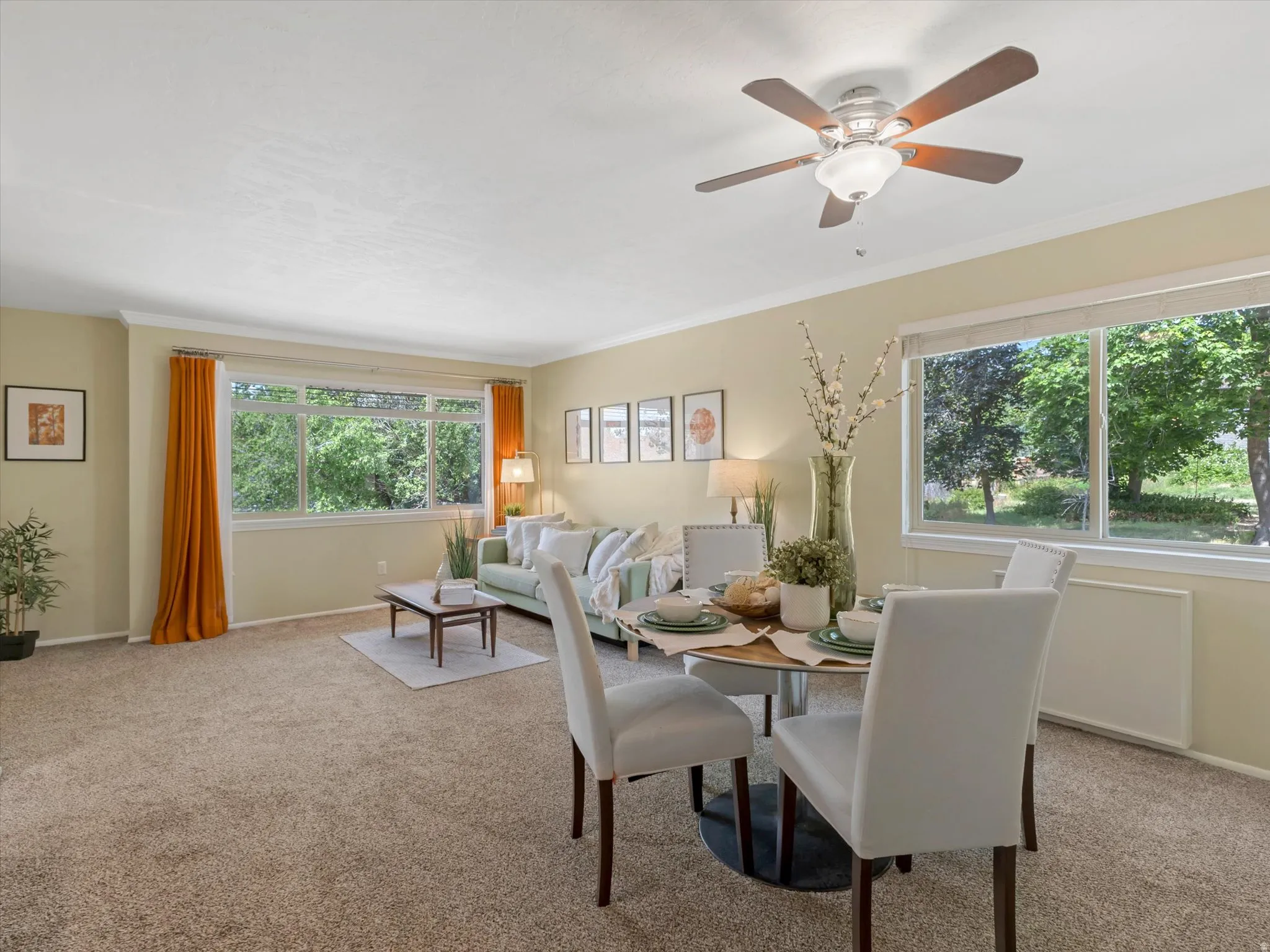 Carpeted living and dining area featuring multiple large windows, crown molding, and a ceiling fan with integrated lighting