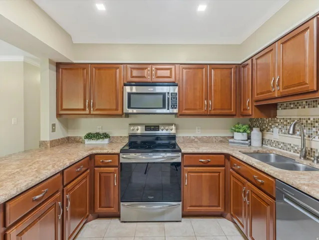 U-shaped kitchen featuring wood cabinetry, stone-look countertops, and a mosaic tile backsplash