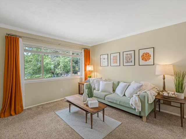 Living area featuring broad window, light beige wall color, crown molding, and carpet flooring