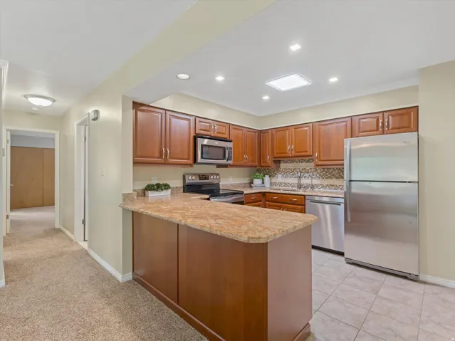 Kitchen featuring wood cabinetry, granite-finish countertops, stainless steel appliances, and a mosaic tile backsplash