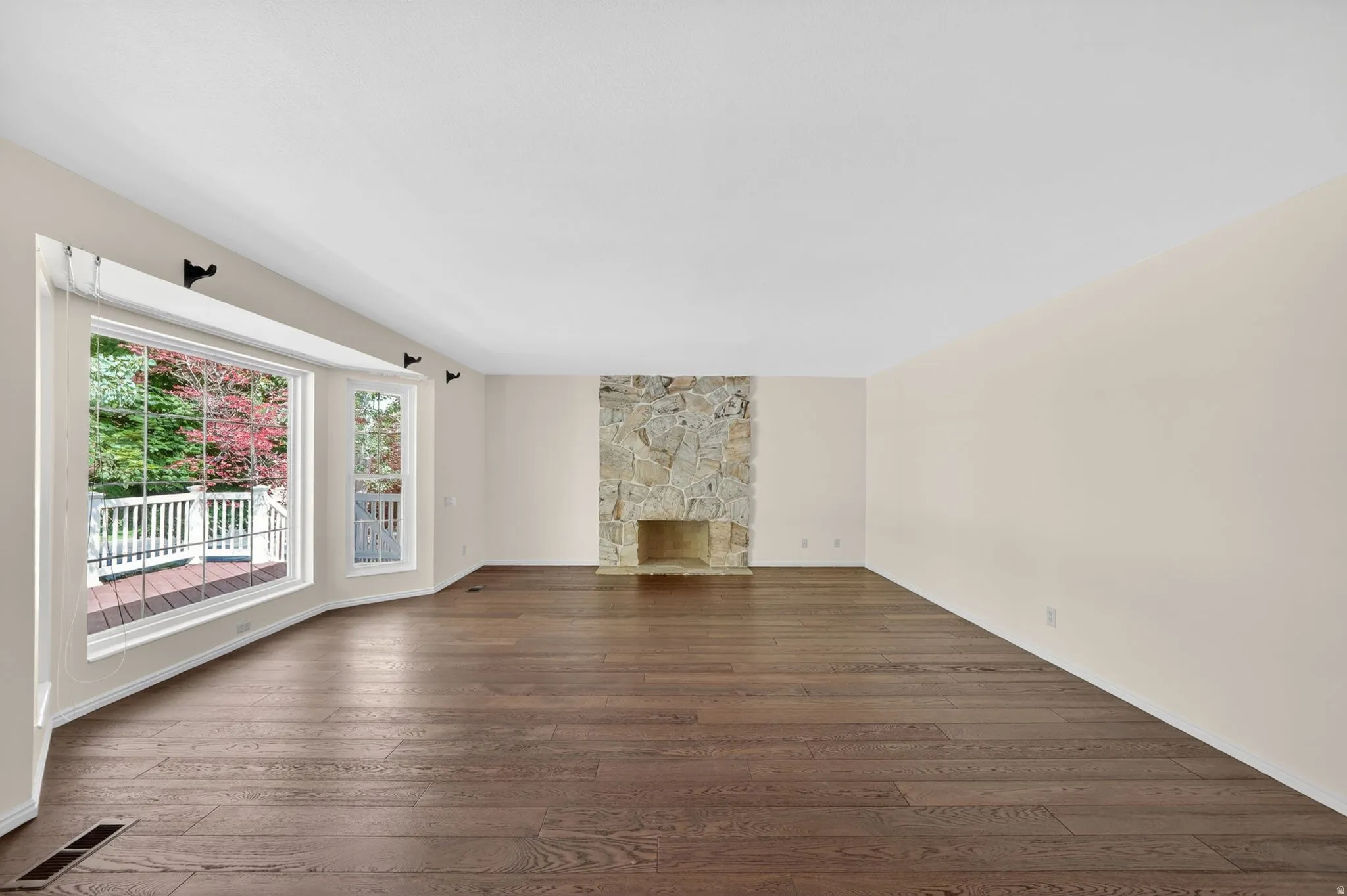 Expansive living area featuring rich wood-finish flooring and a prominent stone fireplace
