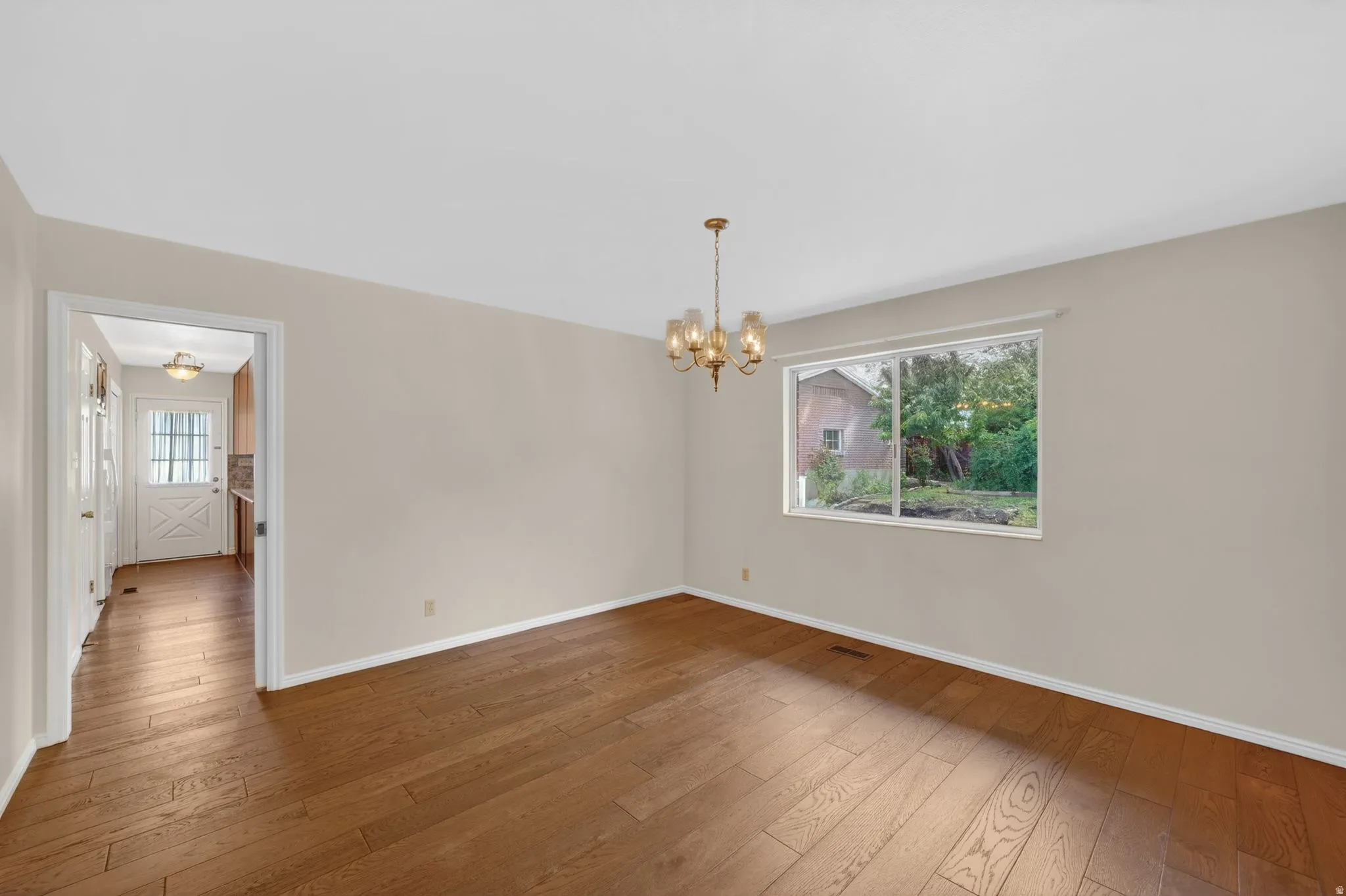 Spacious room featuring wood-finish flooring, a multi-pane window, and a brass chandelier
