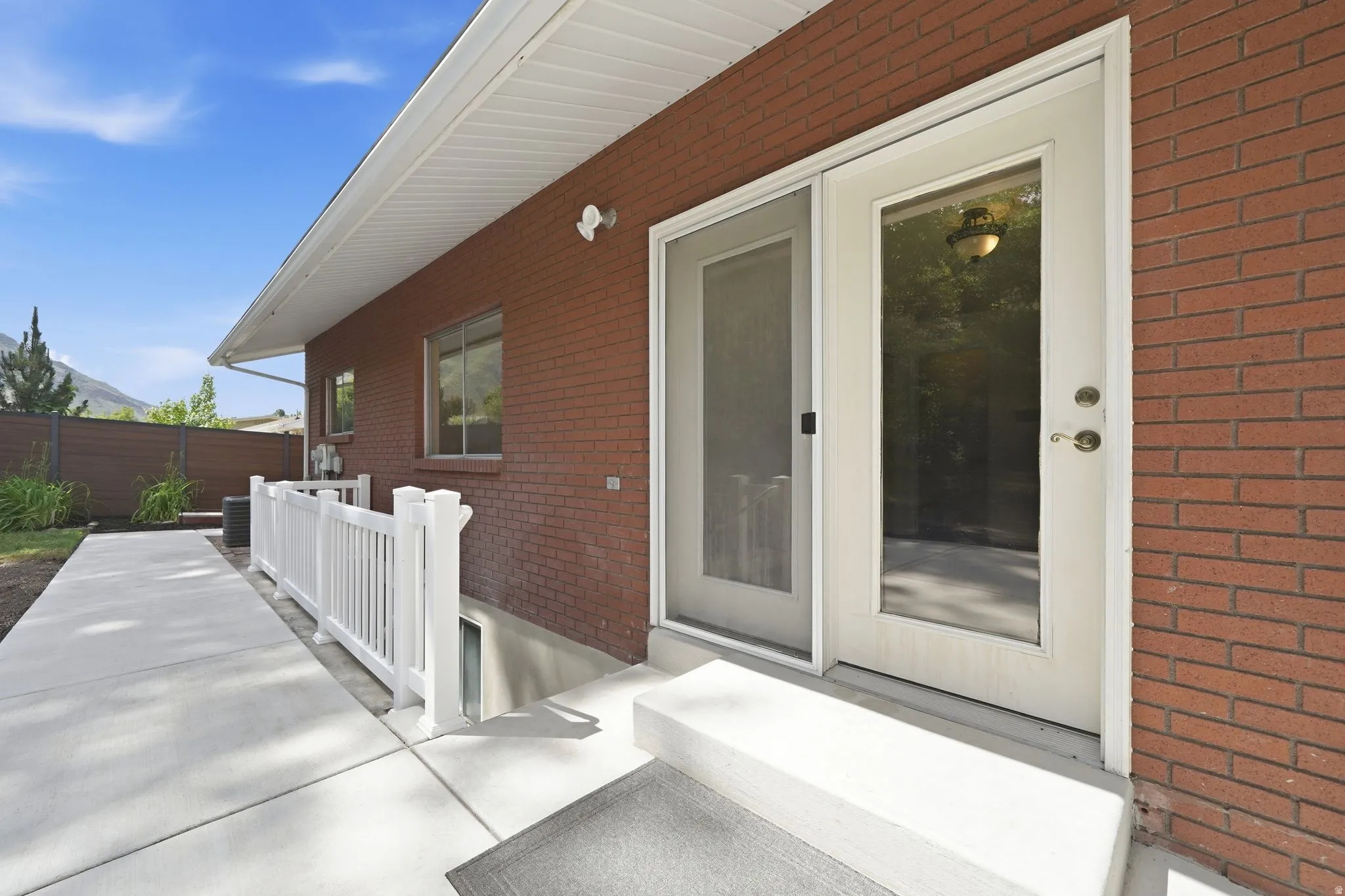 Brick exterior with white trim, concrete walkway, white railing, and a glass-paneled exterior door with a screen door