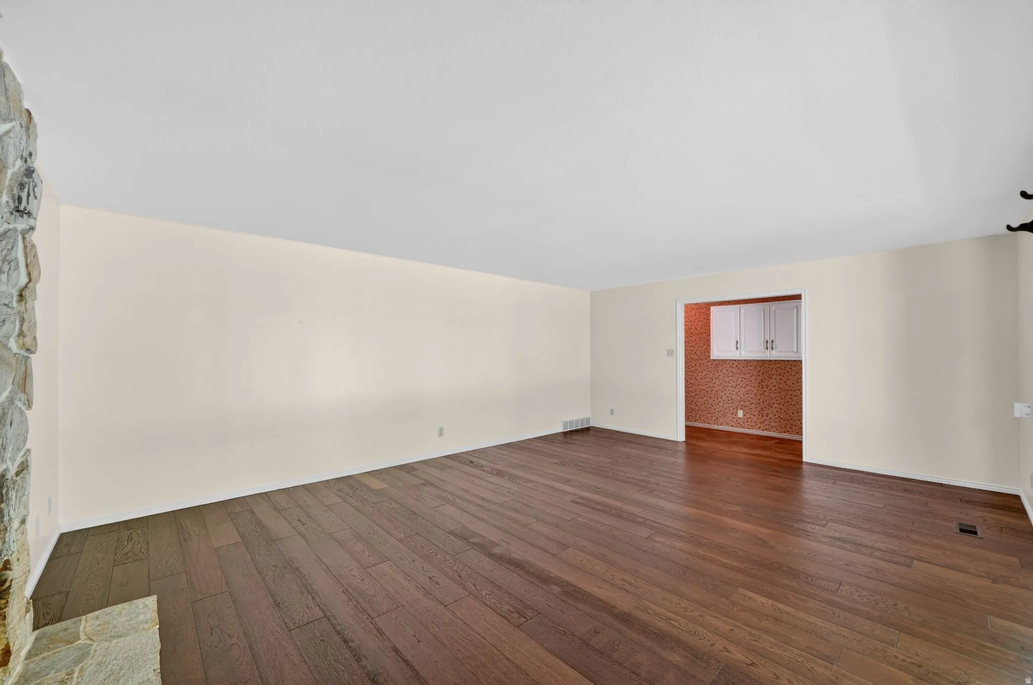 Expansive room featuring rich wood-finish flooring, light-toned walls, and a stone-clad fireplace