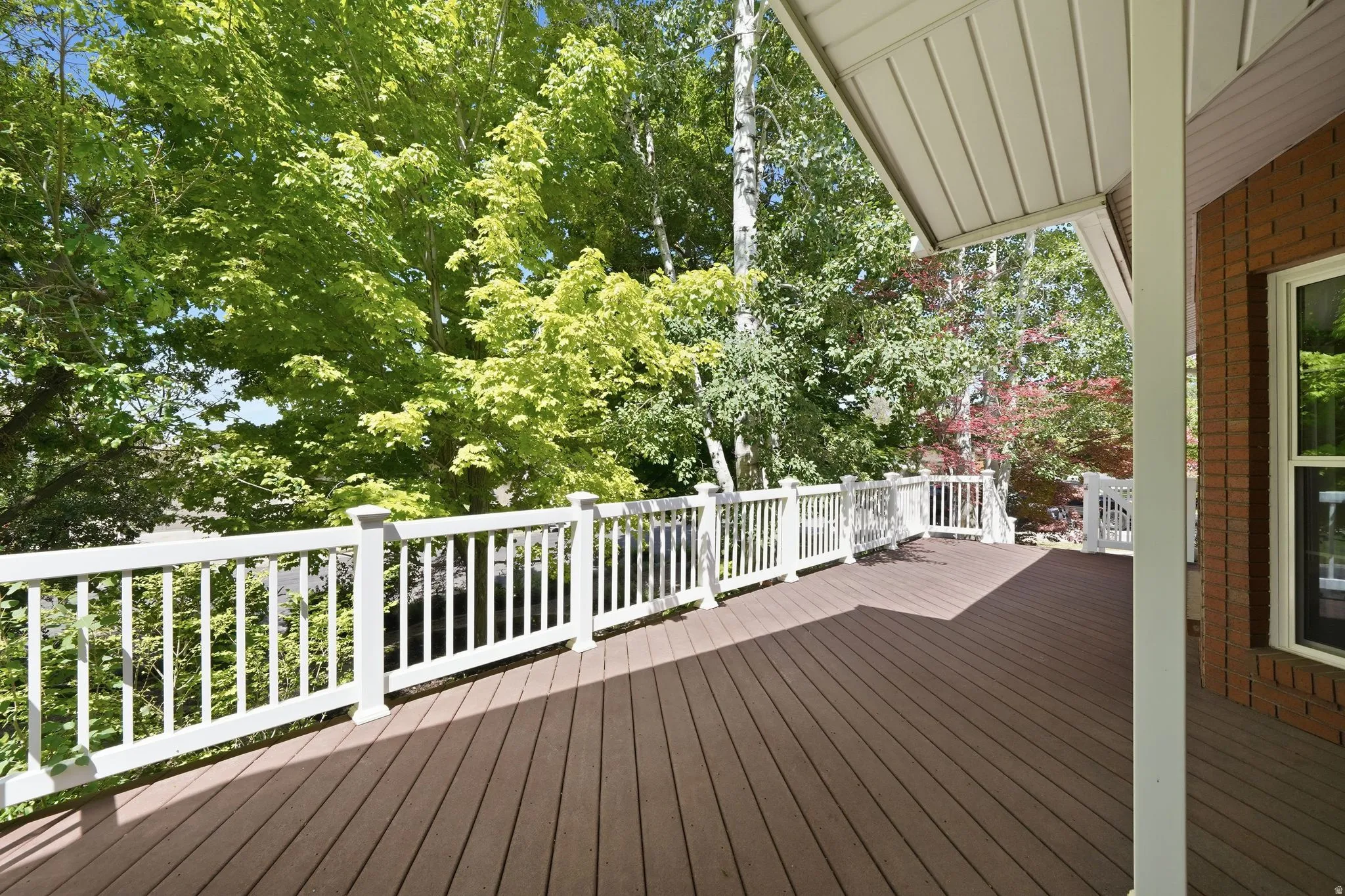 Expansive outdoor deck featuring wood-finish decking, white railings, a covered patio area, and a brick exterior wall