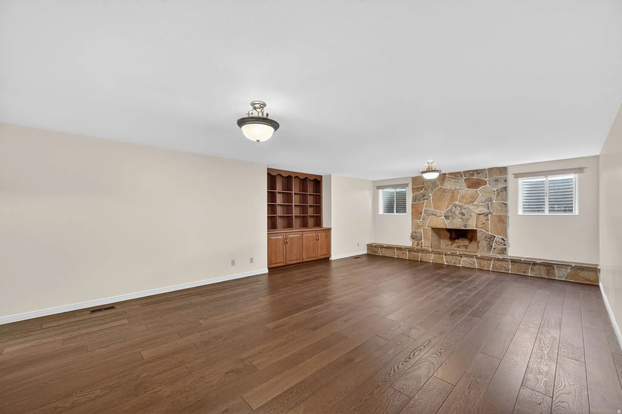 Spacious interior featuring wood-finish flooring, a stone-clad fireplace with a hearth, built-in wooden shelving, and recessed windows