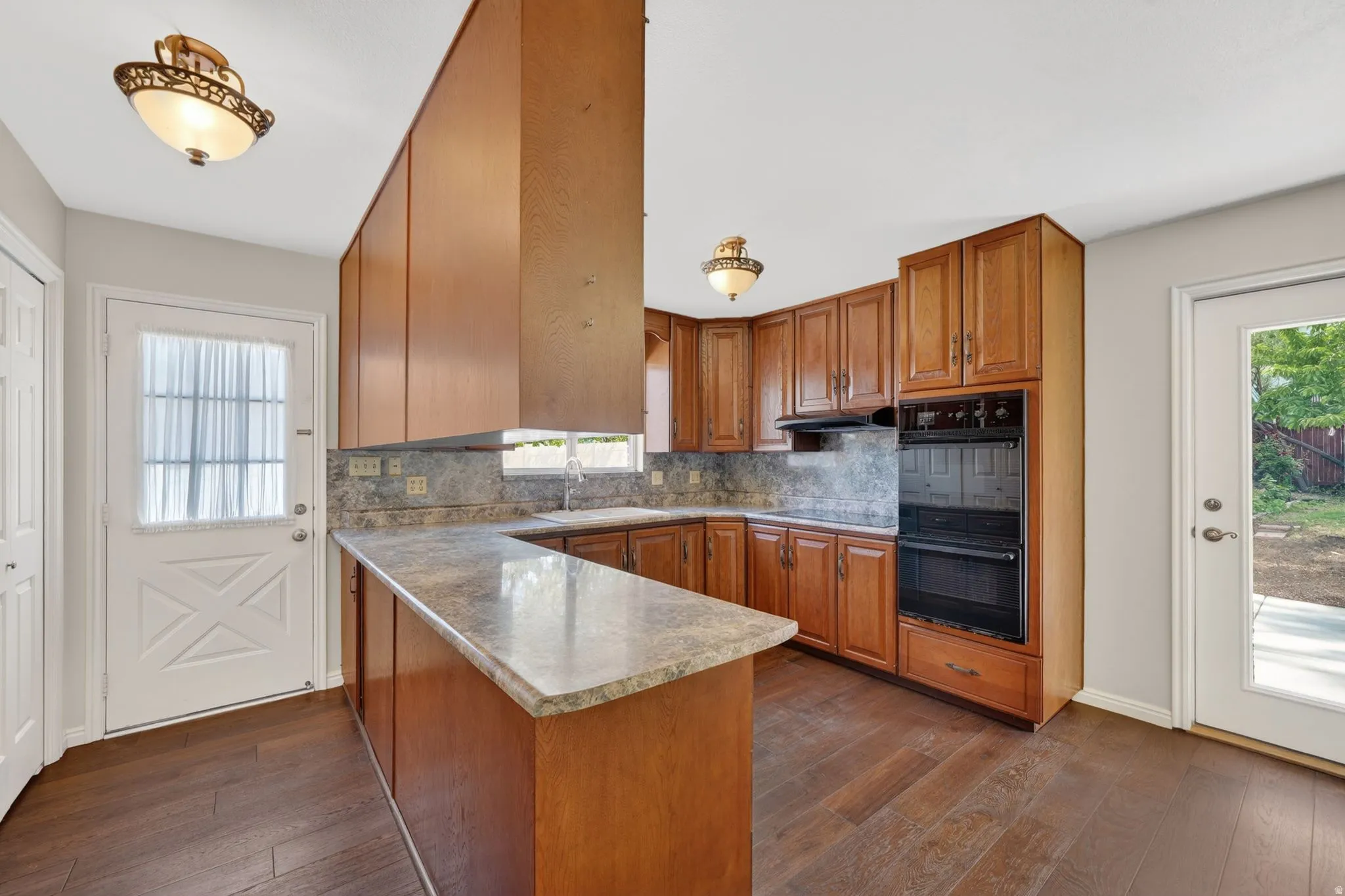 Kitchen featuring wood-finish flooring, wood cabinetry, stone-look countertops, and a built-in double oven