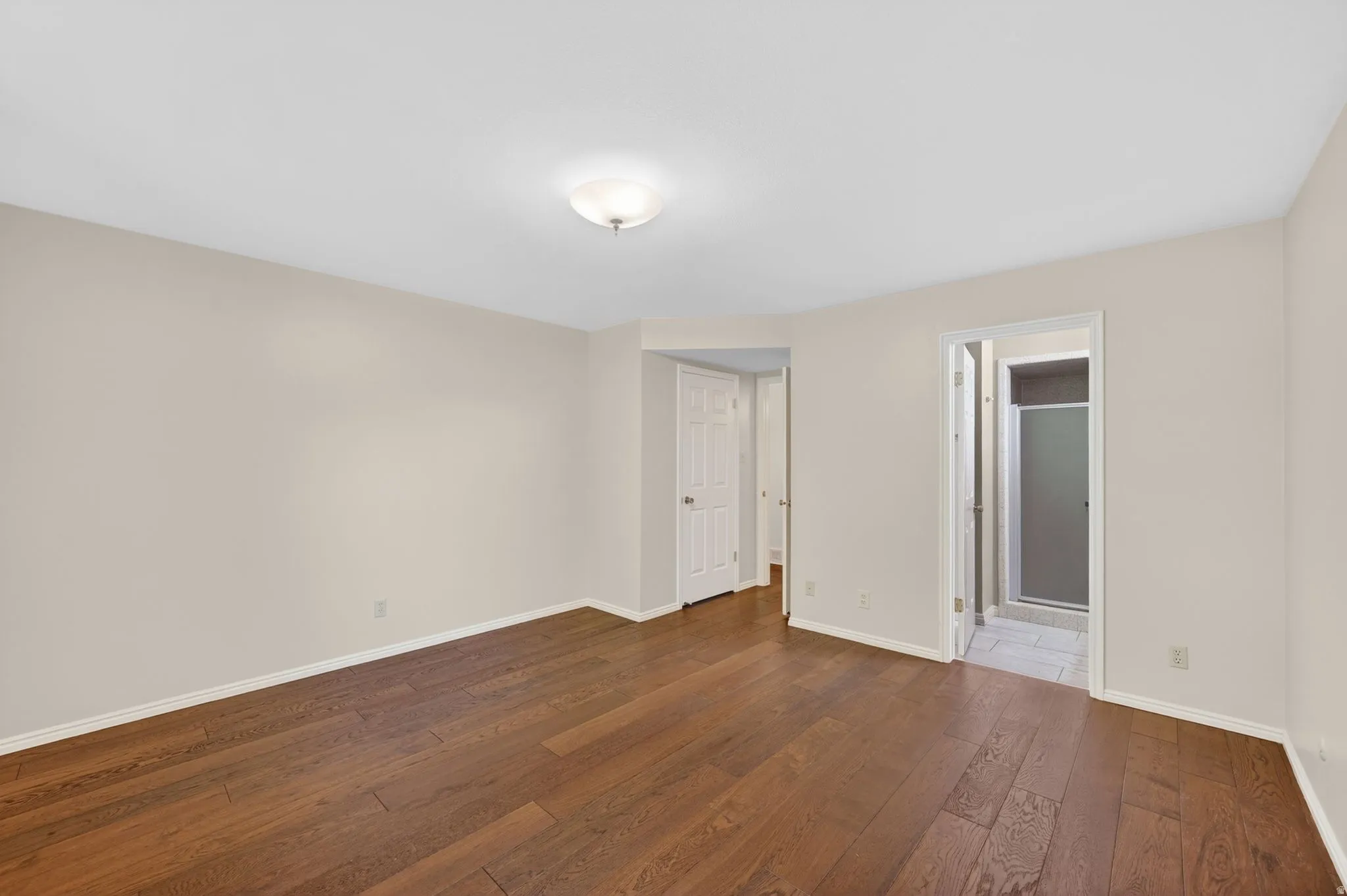 Spacious room featuring wood-finish flooring, light neutral wall tones, and a flush-mount ceiling light