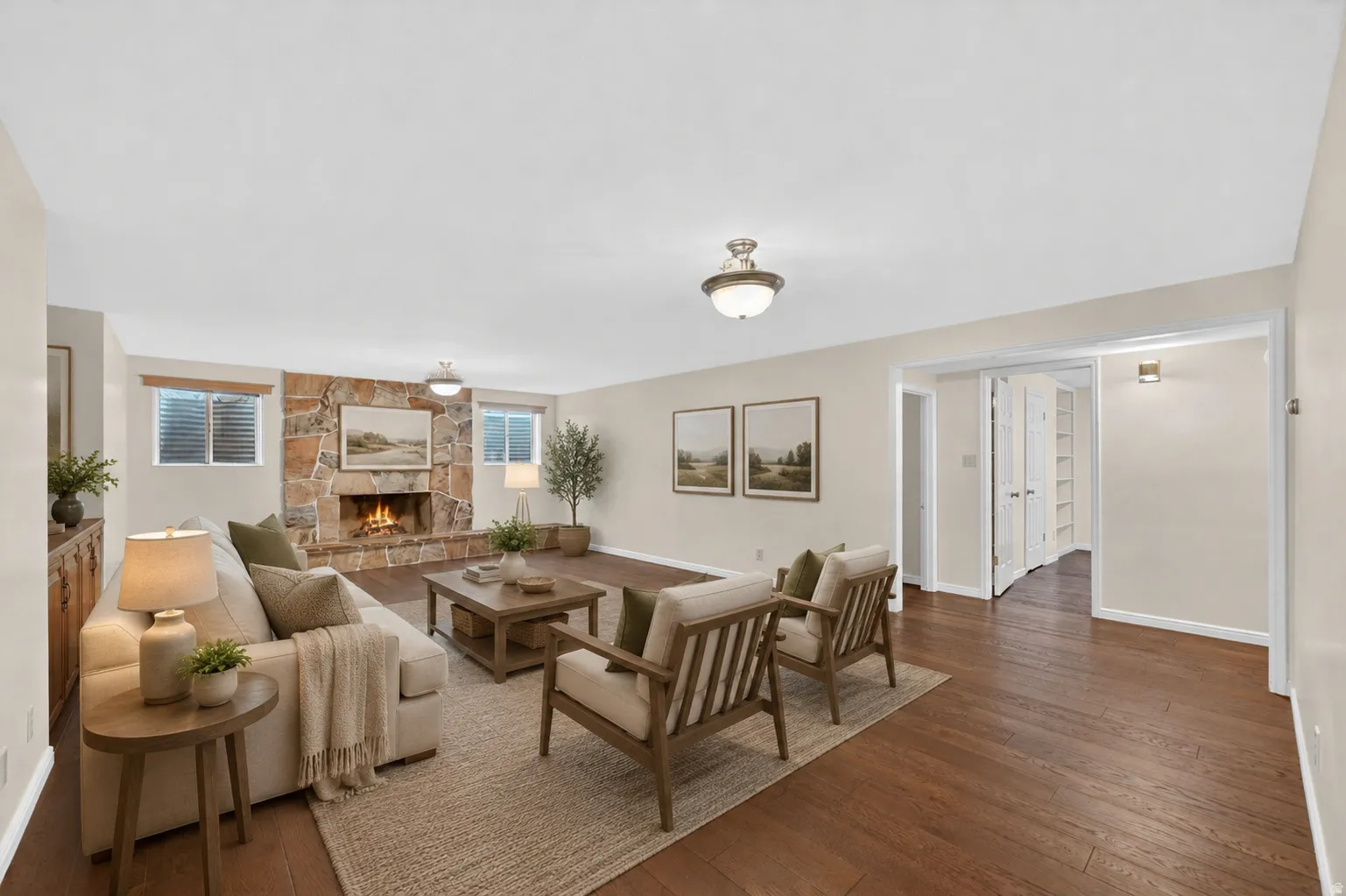 Spacious living area featuring wood-finish flooring, a stone-clad fireplace, and neutral wall tones