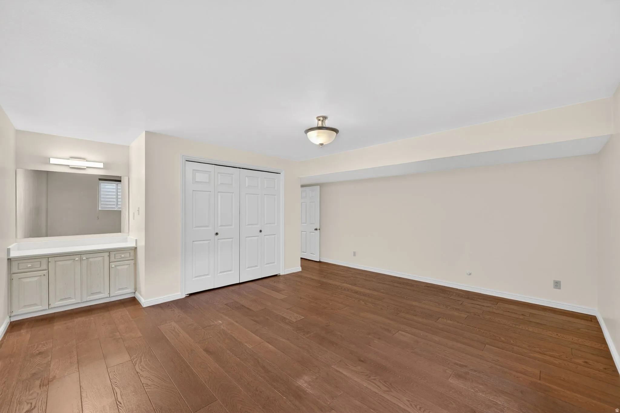 Spacious room featuring wood-finish flooring, a built-in vanity with cabinetry and countertop, an integrated mirror with sconce lighting, and bi-fold closet doors