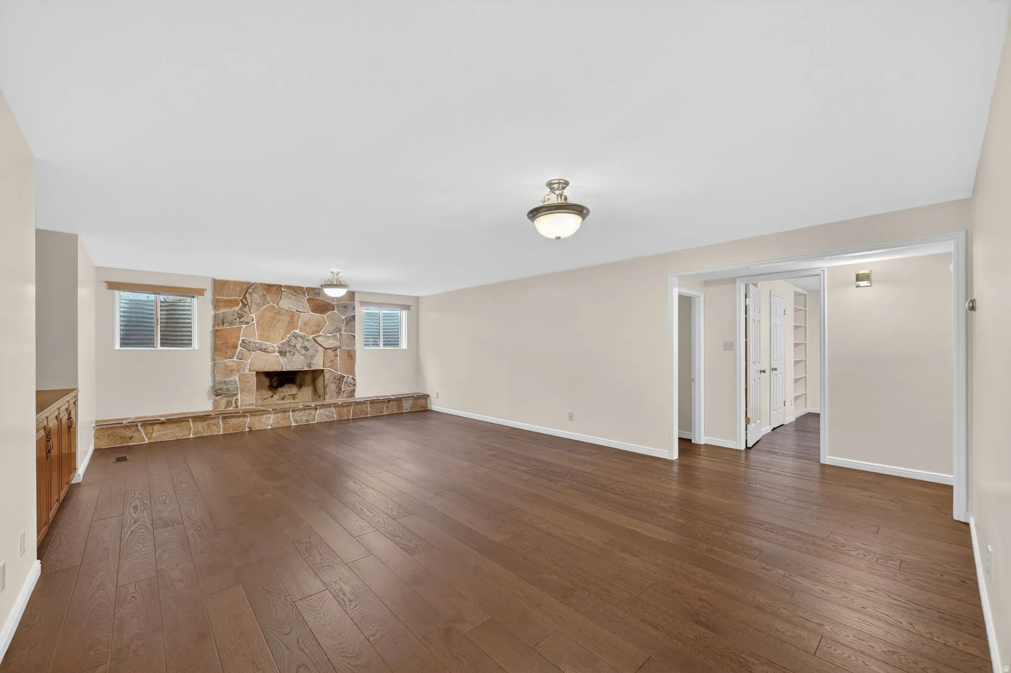 Spacious room featuring wood-finish flooring, a stone-clad fireplace with a stone hearth, and two windows with blinds