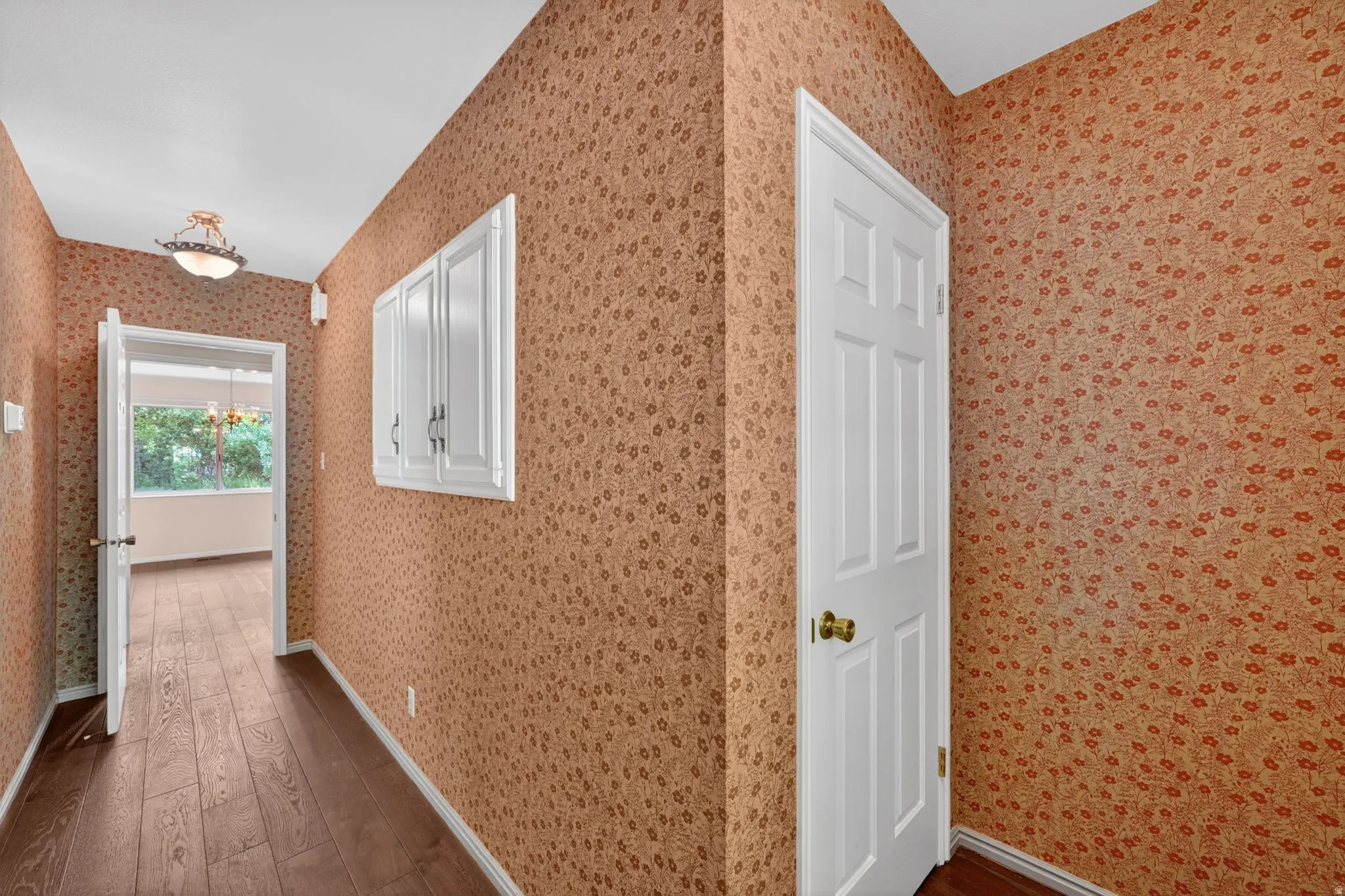 Hallway featuring wood-finish flooring, patterned wallpaper, white trim, and a semi-flush mount light fixture