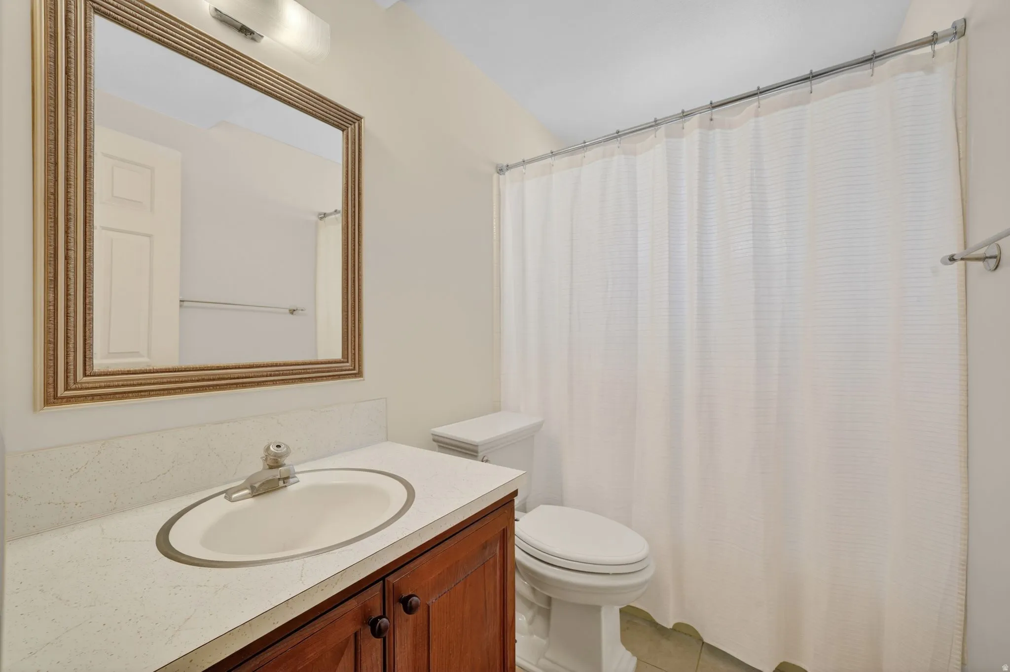 Bathroom featuring a wood-finish vanity with a light-toned countertop, an undermount sink, and a framed mirror