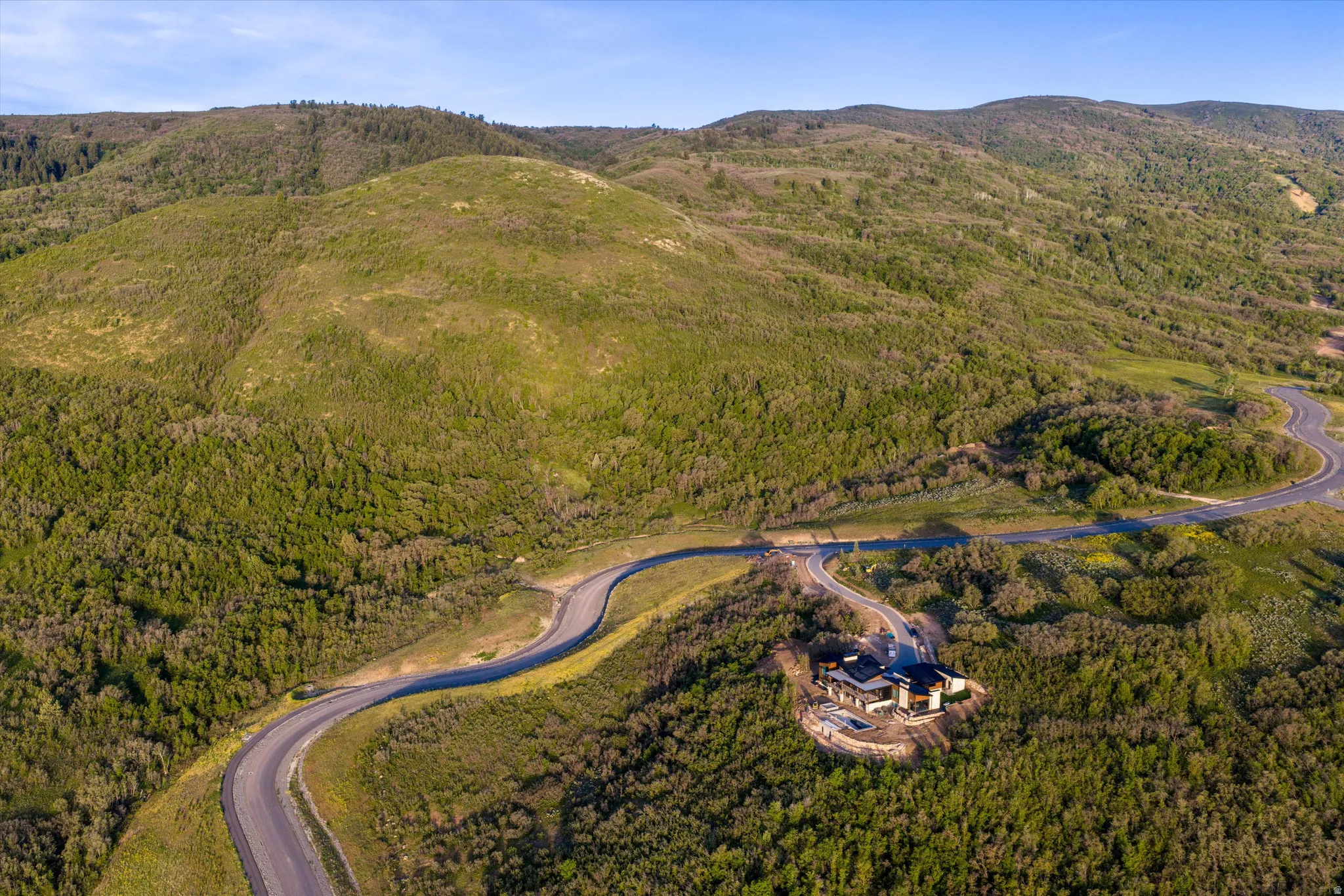Property situated amidst expansive green hills, accessible via a winding paved road