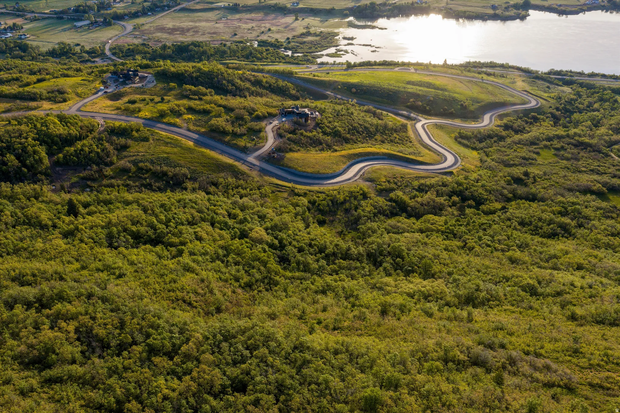 Winding paved road traversing rolling hills with surrounding green foliage and distant water