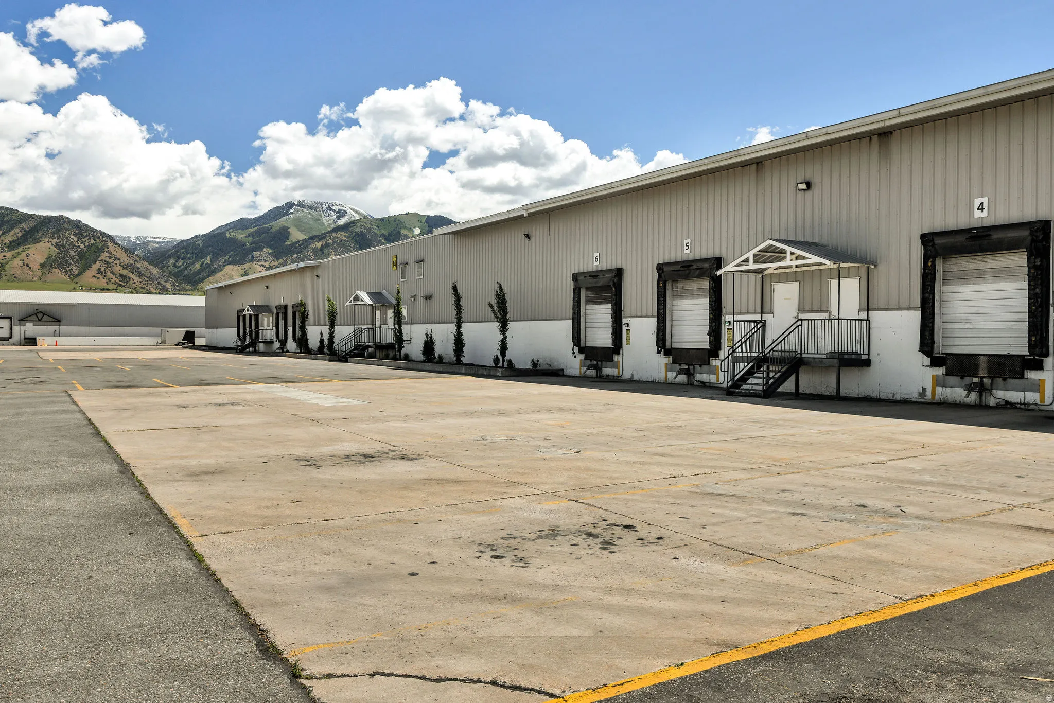 Commercial property featuring multiple loading dock doors, a dedicated pedestrian entrance with an awning, an expansive paved lot, and a corrugated metal exterior