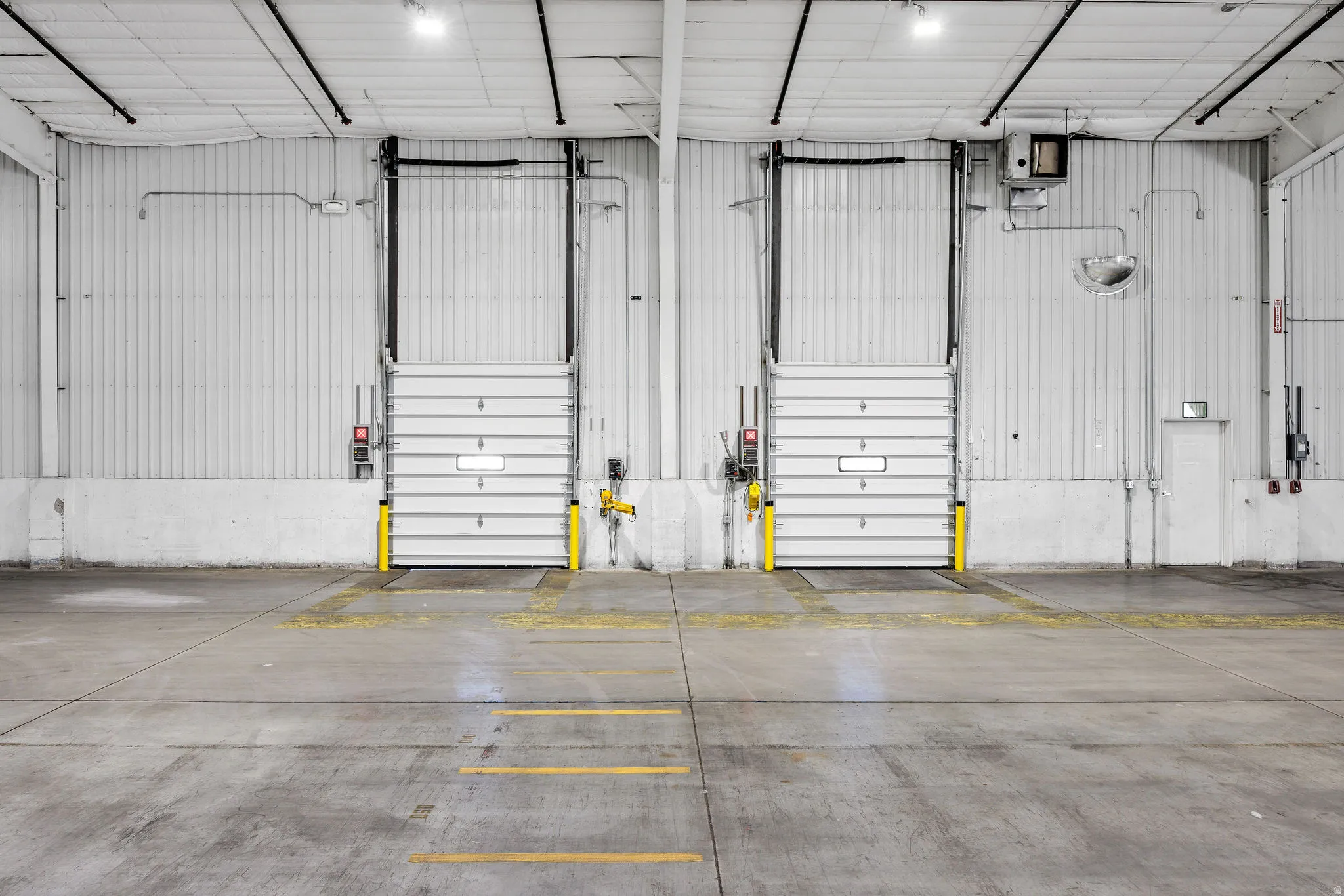 Concrete floor with yellow directional markings and two industrial roll-up doors