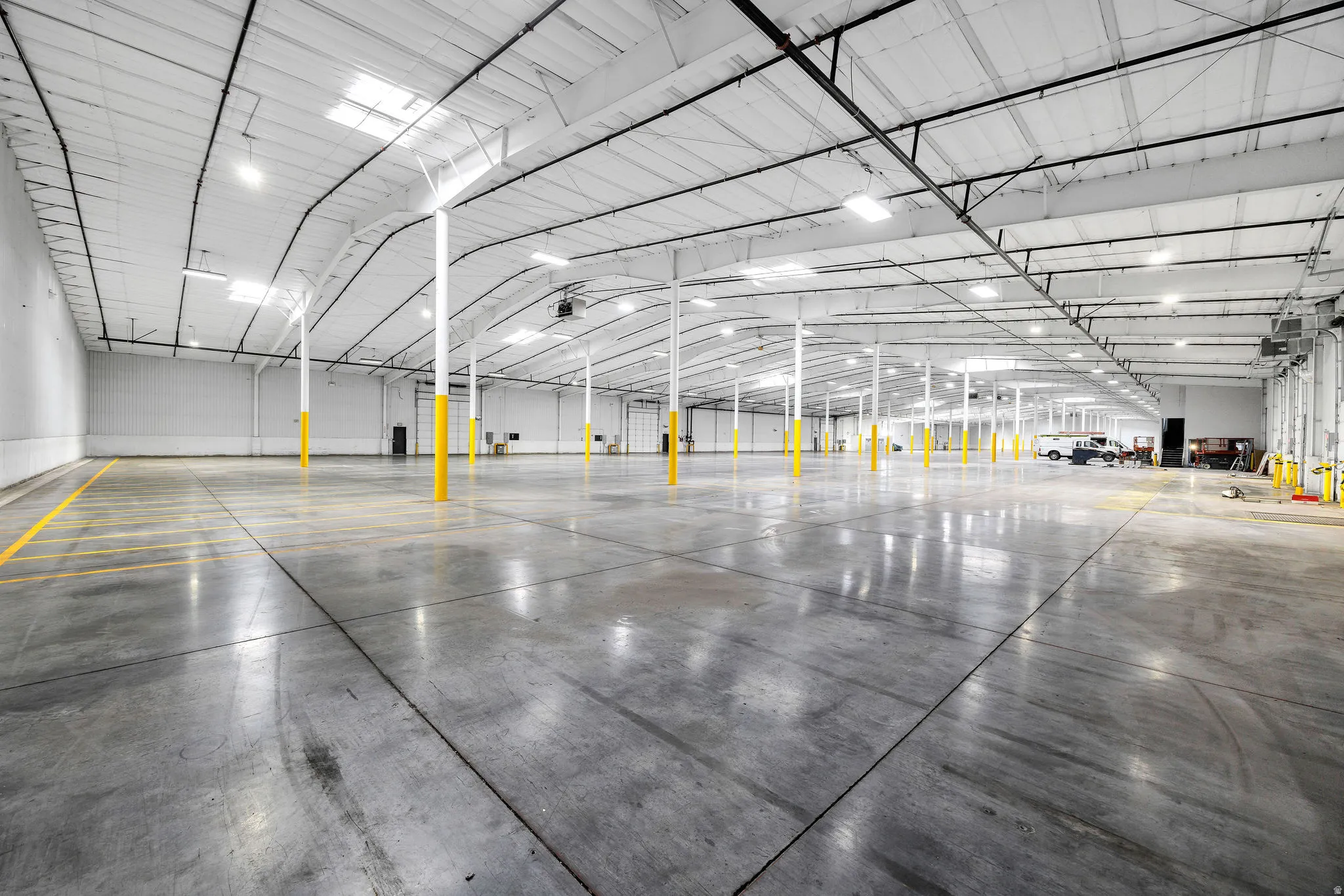 Spacious commercial warehouse featuring polished concrete flooring, high ceilings with exposed trusses, multiple skylights, overhead lighting, and prominent support columns