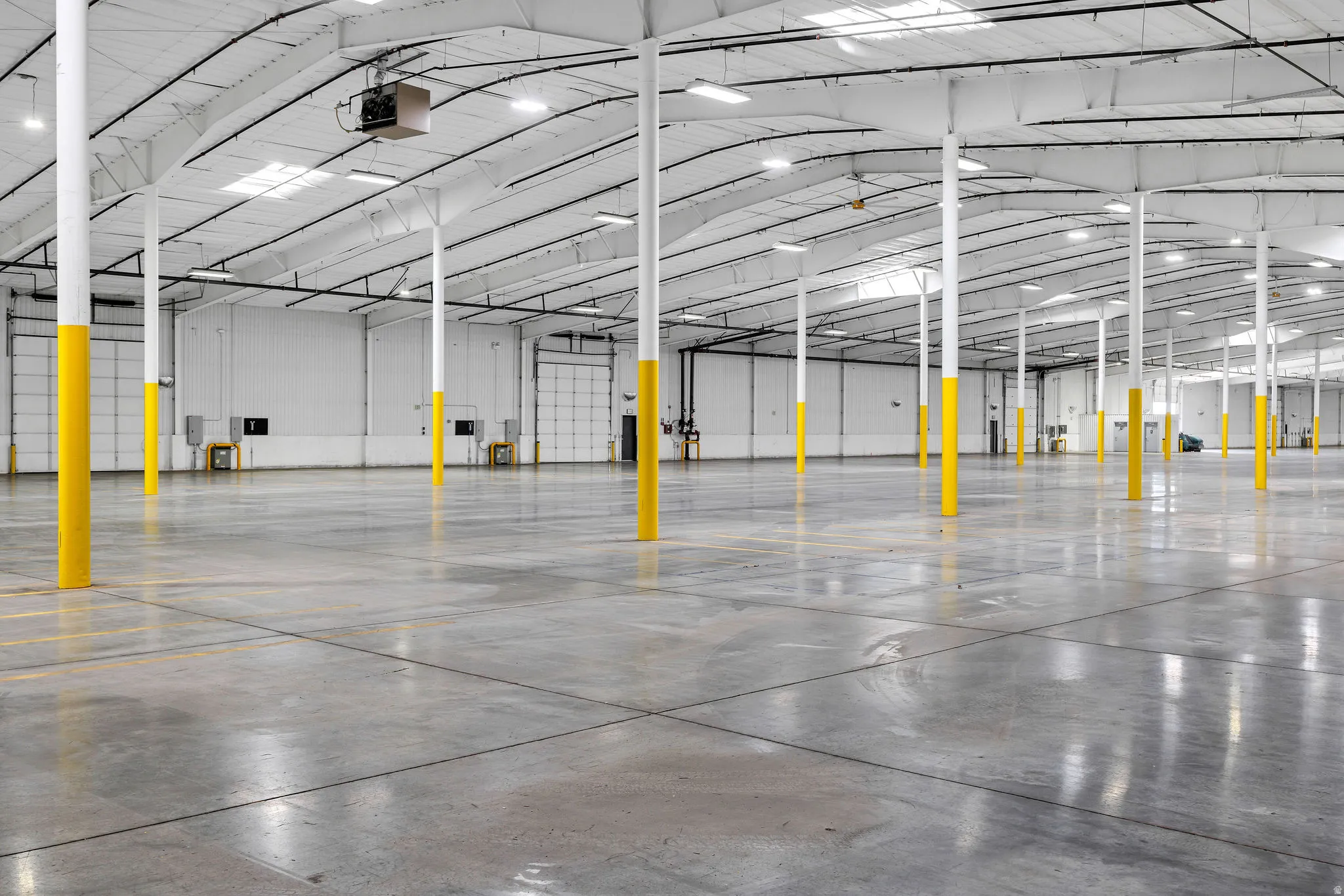 Expansive industrial warehouse featuring polished concrete flooring, numerous support columns, and multiple overhead doors