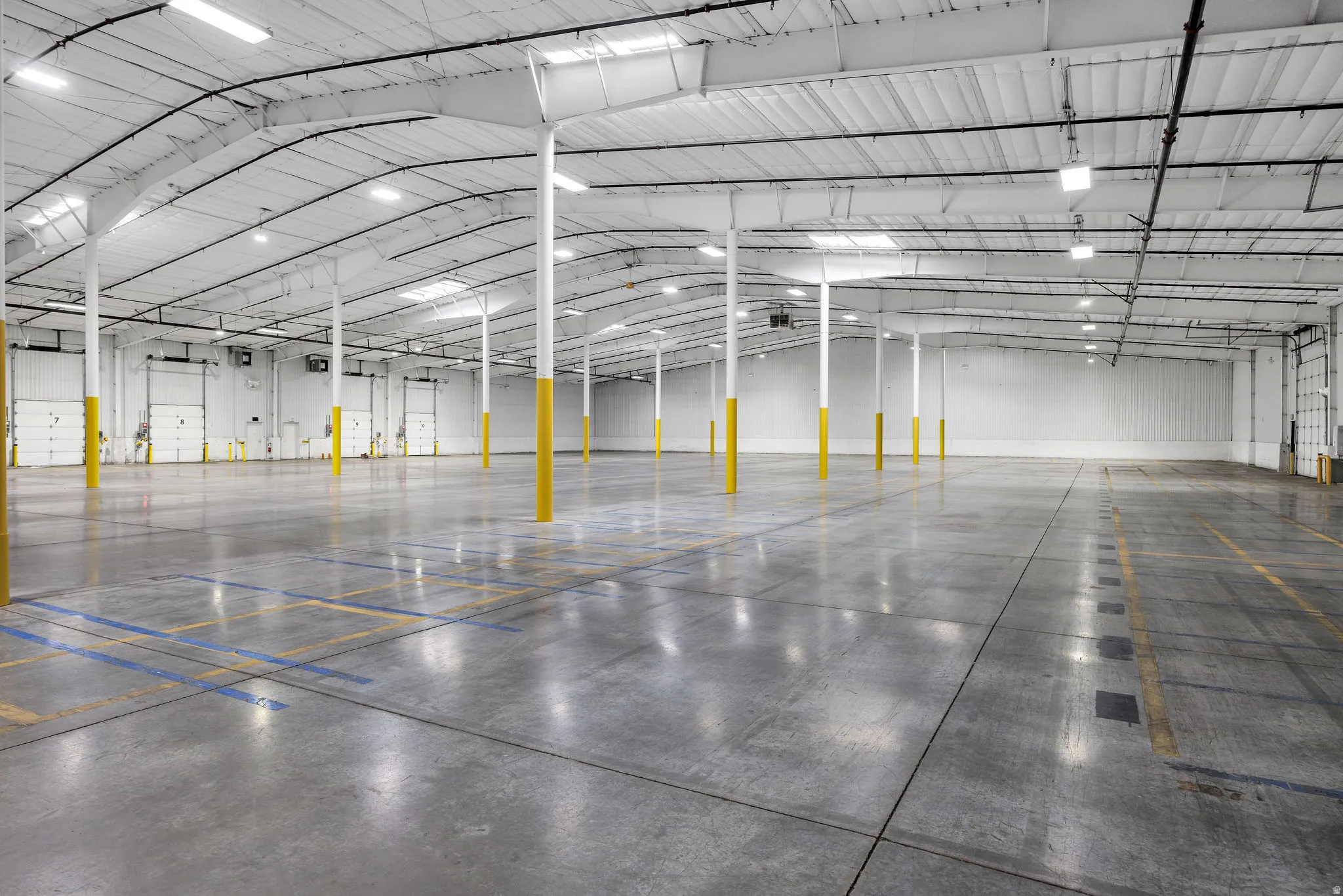 Spacious warehouse interior featuring a high arched ceiling with exposed metal trusses, multiple skylights, and fluorescent lighting
