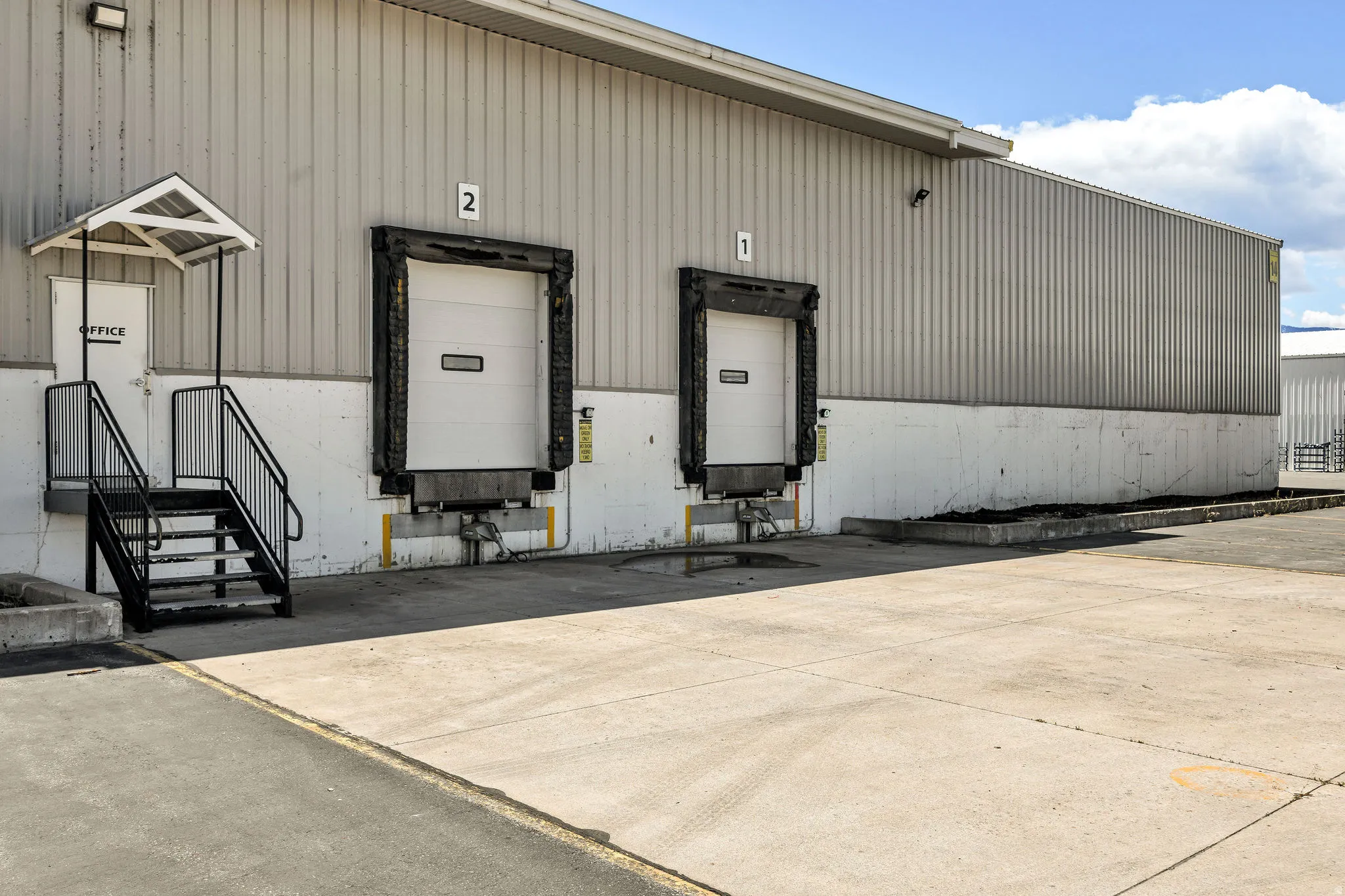 Commercial building featuring two overhead bay doors with loading docks, an exterior office entrance with stairs and railing, and a corrugated metal facade