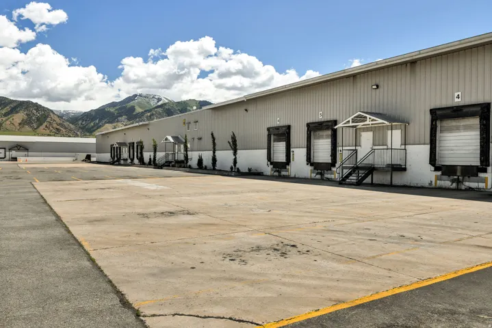 Commercial property featuring multiple loading dock doors, a dedicated pedestrian entrance with an awning, an expansive paved lot, and a corrugated metal exterior