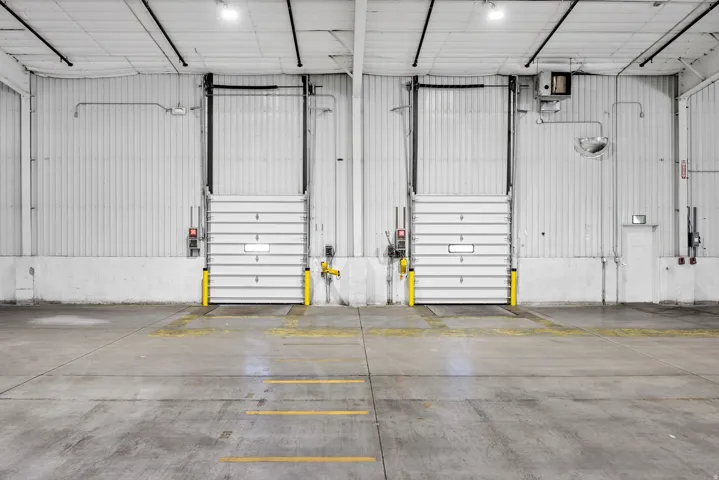 Concrete floor with yellow directional markings and two industrial roll-up doors